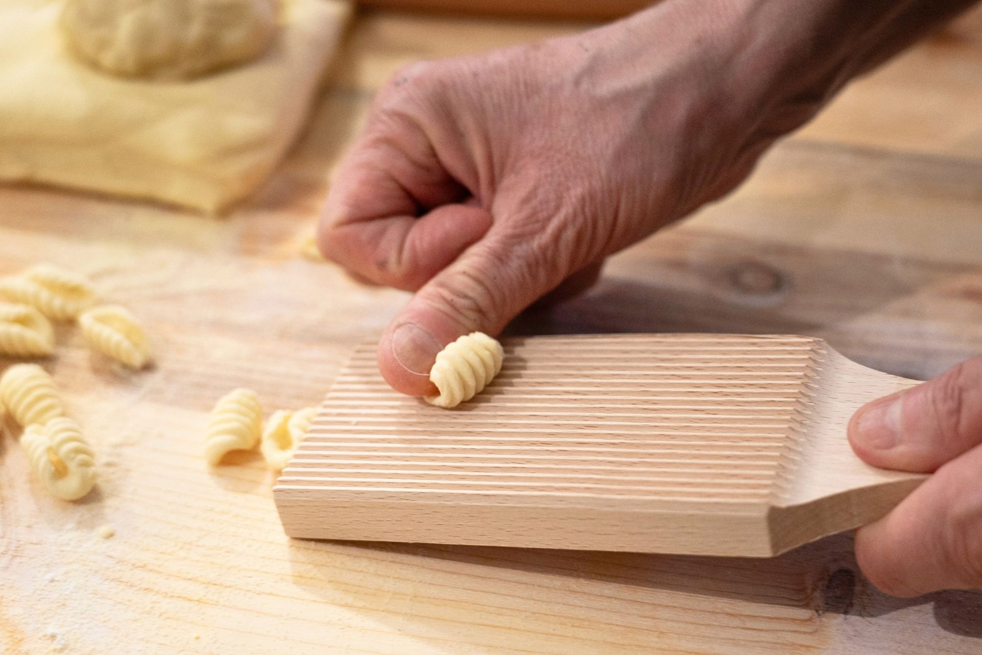Una persona che lavora pasta fresca con un attrezzo in legno su un tavolo di legno.
