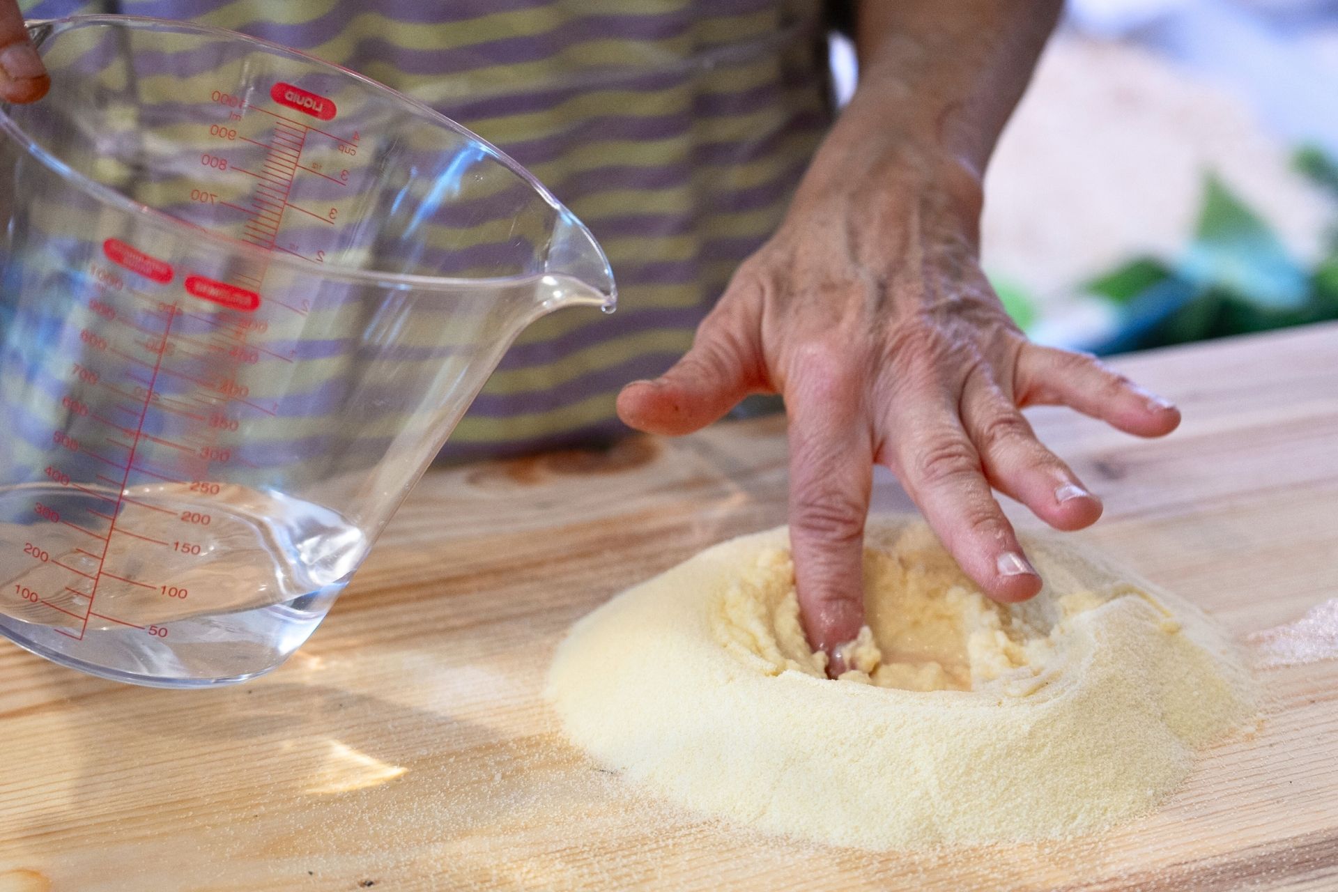 Una persona versa acqua in una ciotola con farina per preparare la pasta fresca in un laboratorio ad Alghero.