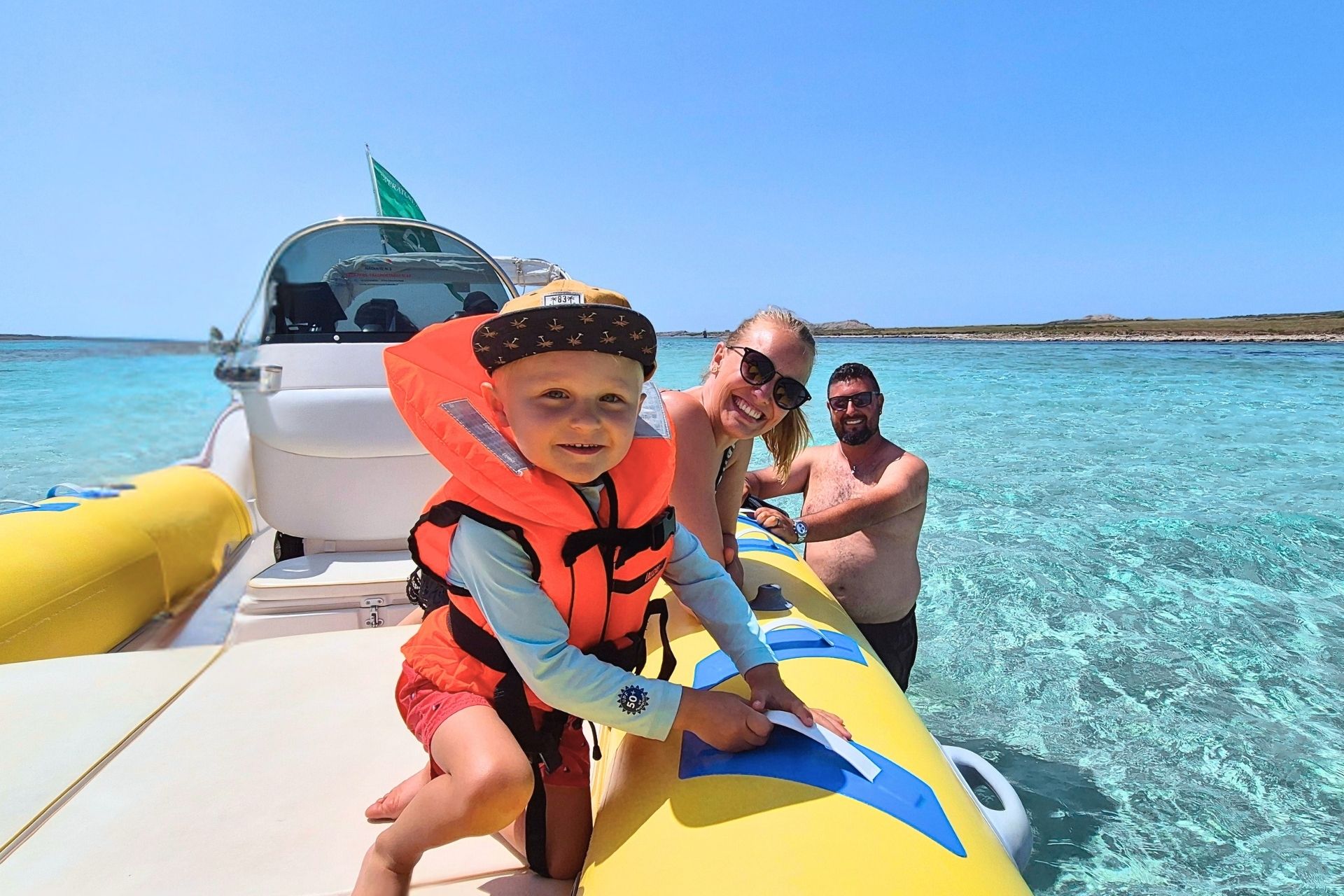 Family in a dinghy near the coast with crystal clear sea and white sand beach