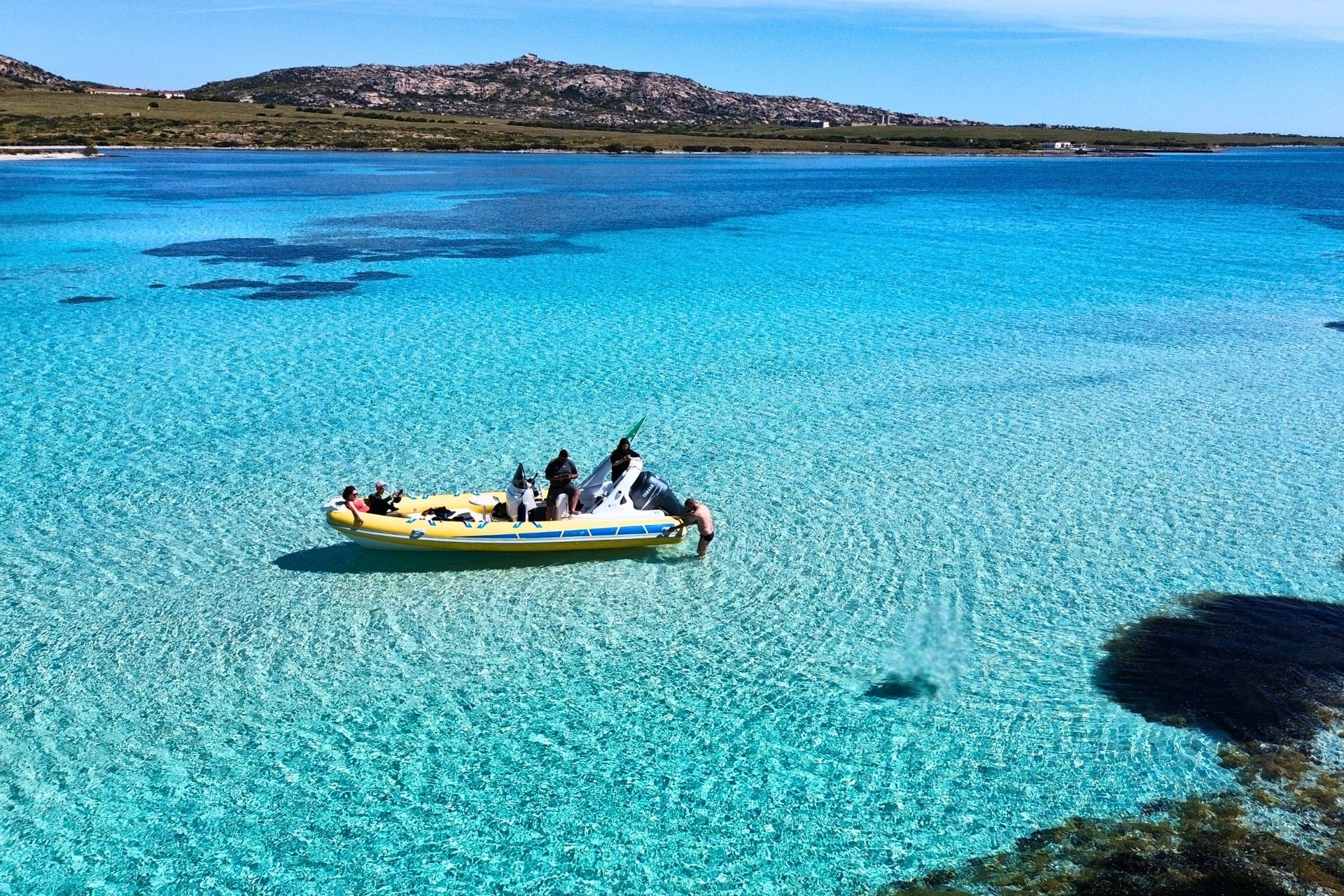 Group of people in a dinghy in the blue and transparent sea, near the coast