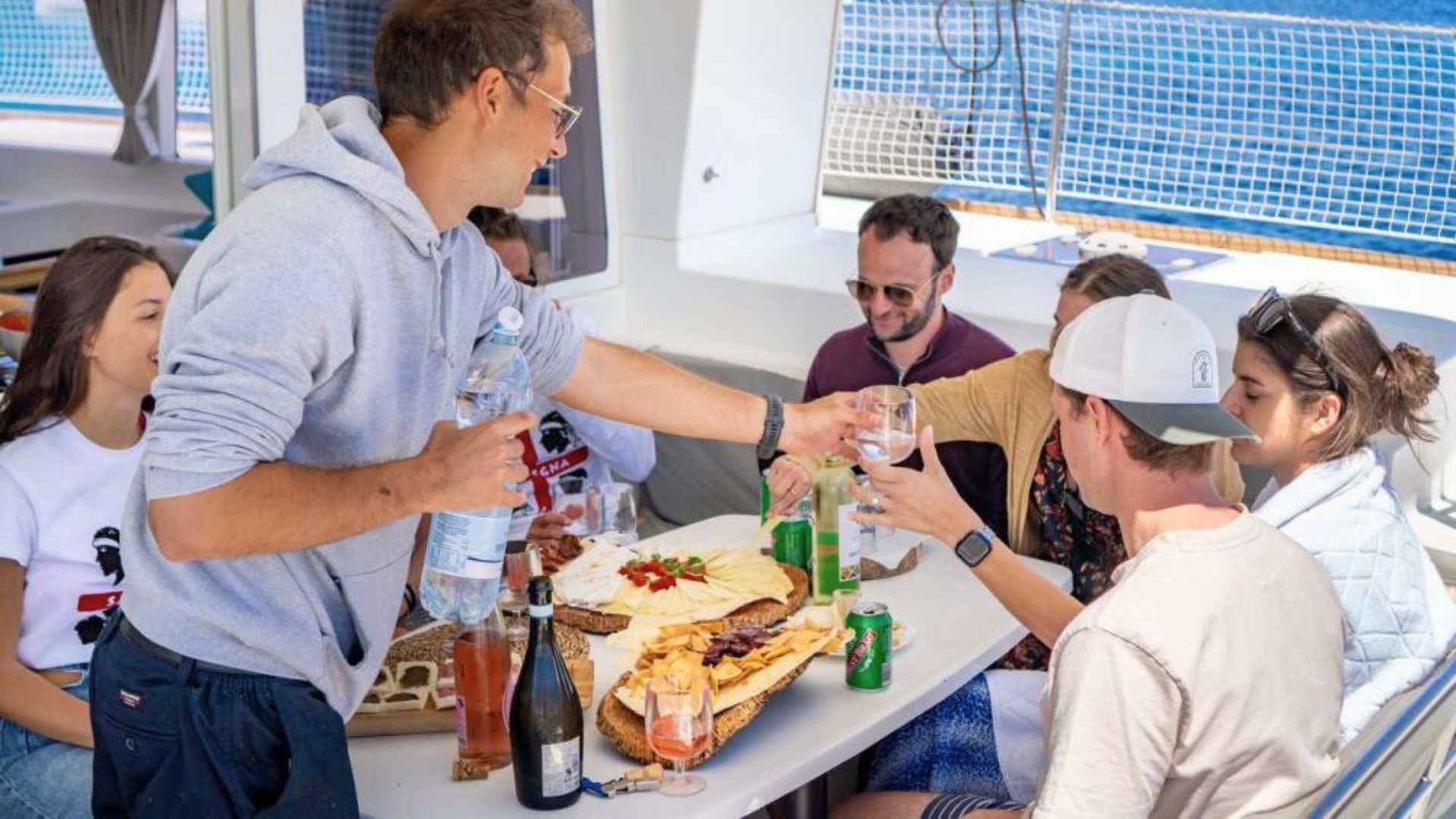 Groupe de personnes assises à une table sur le catamaran avec de la nourriture et des boissons devant le