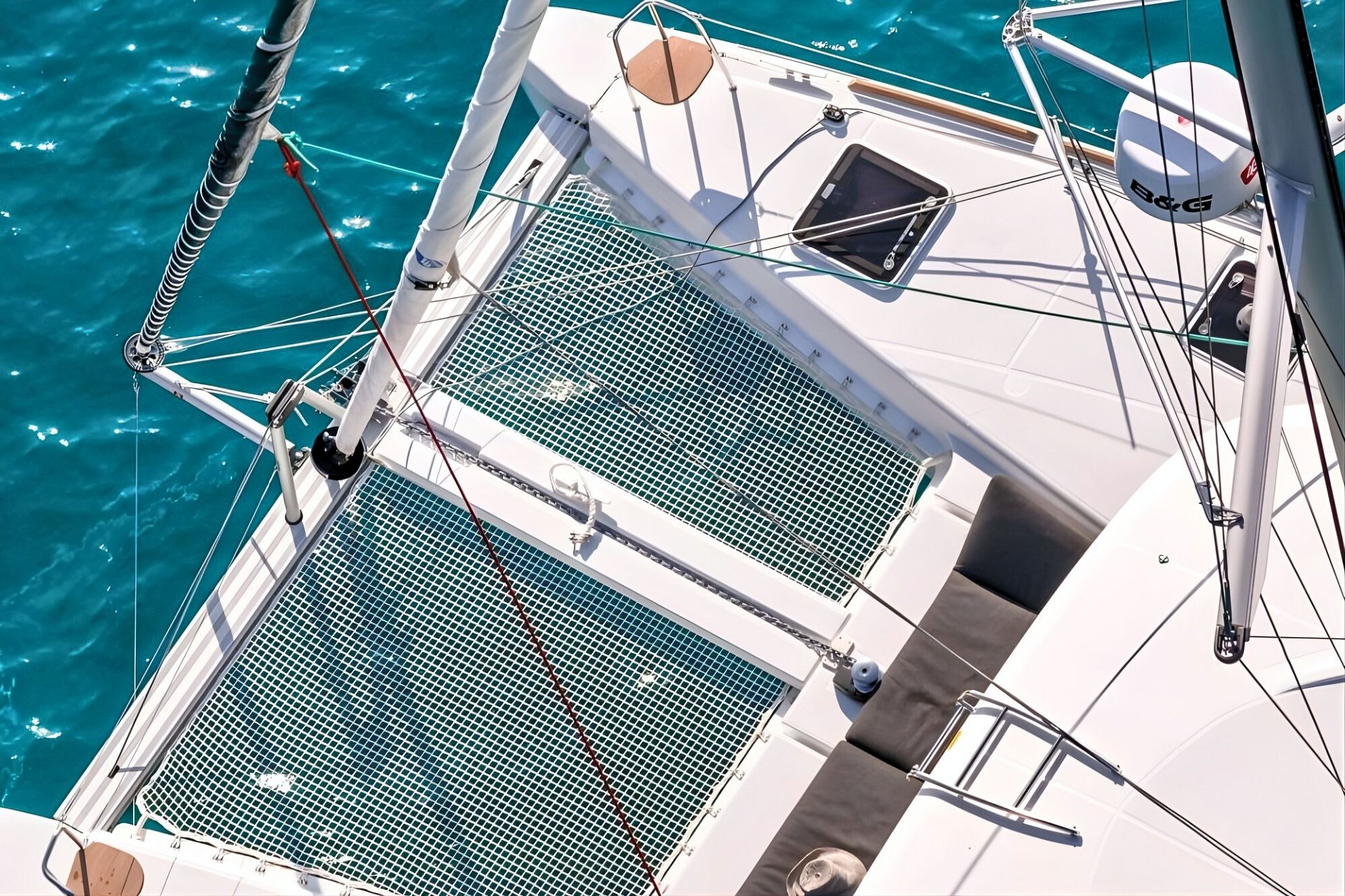 Imagen de un catamarán con una red de protección en la cubierta y un área de relajación con cojines, en aguas tranquilas y cristalinas.