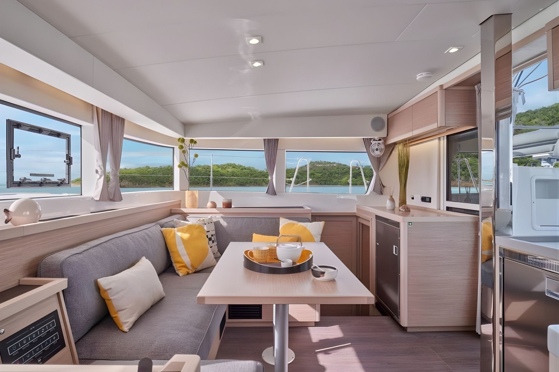 Interior de un catamarán con mesa, sofá y vistas al mar y las islas circundantes.