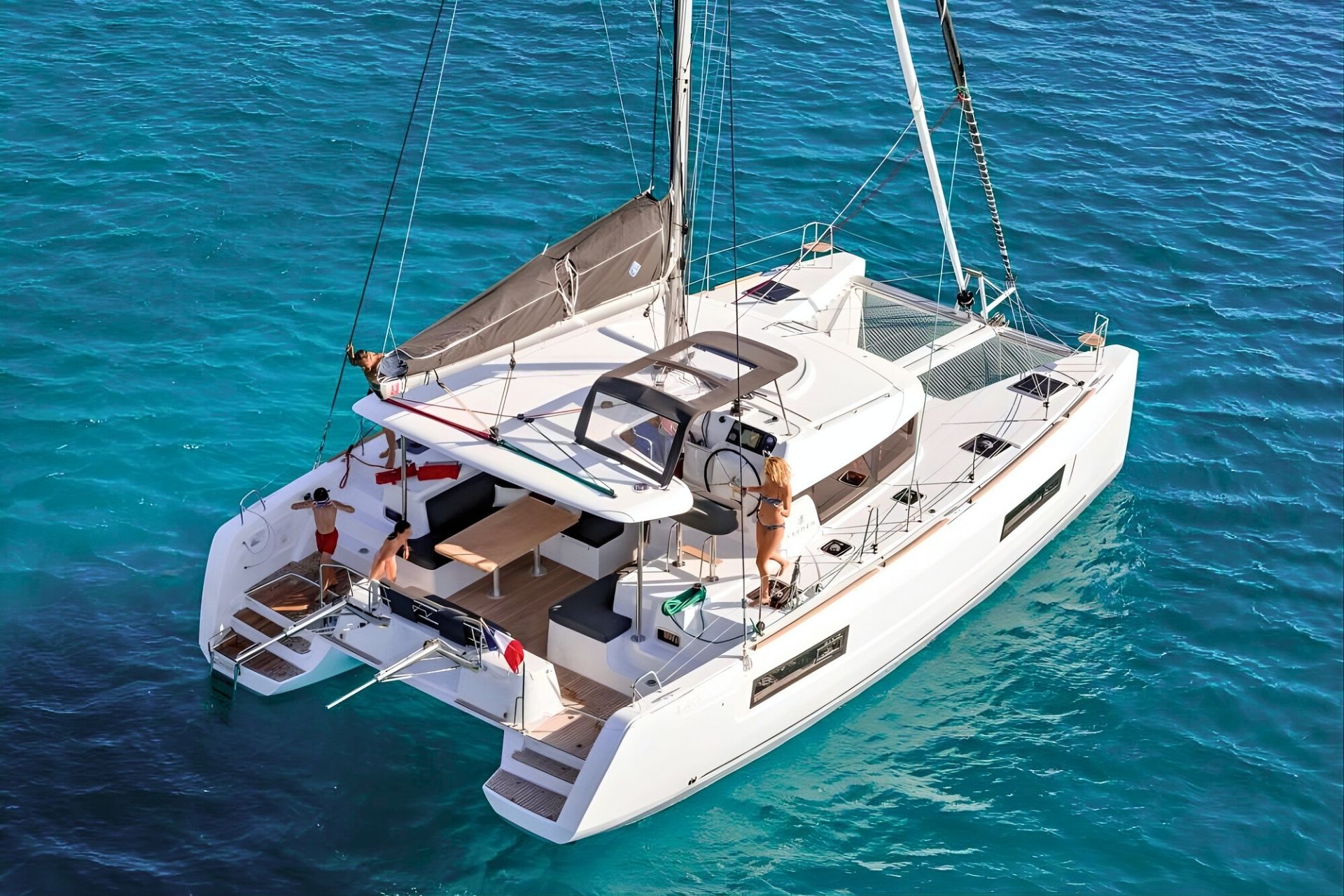 Navegación en catamarán con personas a bordo y otras en el agua, en el mar azul.