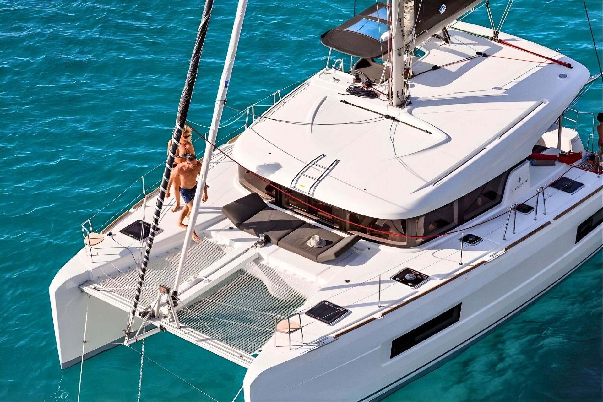 Catamarán con dos personas a bordo y otras dos personas en el agua junto al barco