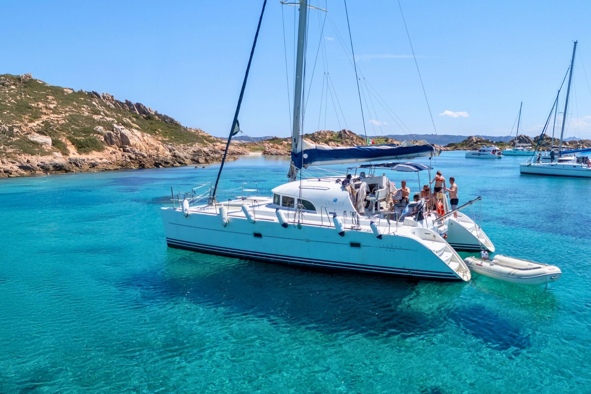 A luxurious catamaran sails between the islands of the La Maddalena Archipelago, departing from Cannigione, offering breathtaking views and opportunities to swim in crystal clear bays.