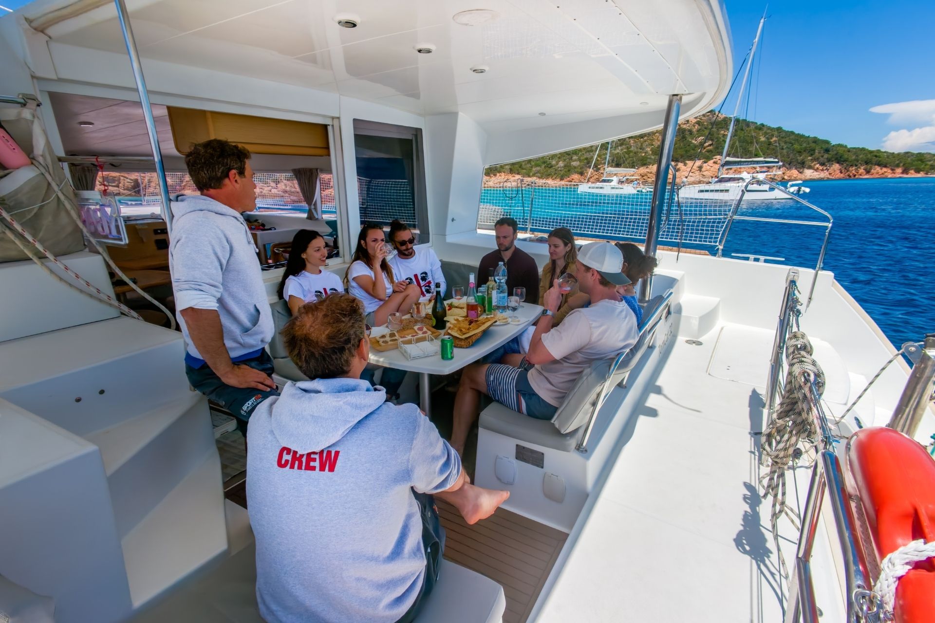 Group of people seated at a table on a catamaran, with a seascape in the background