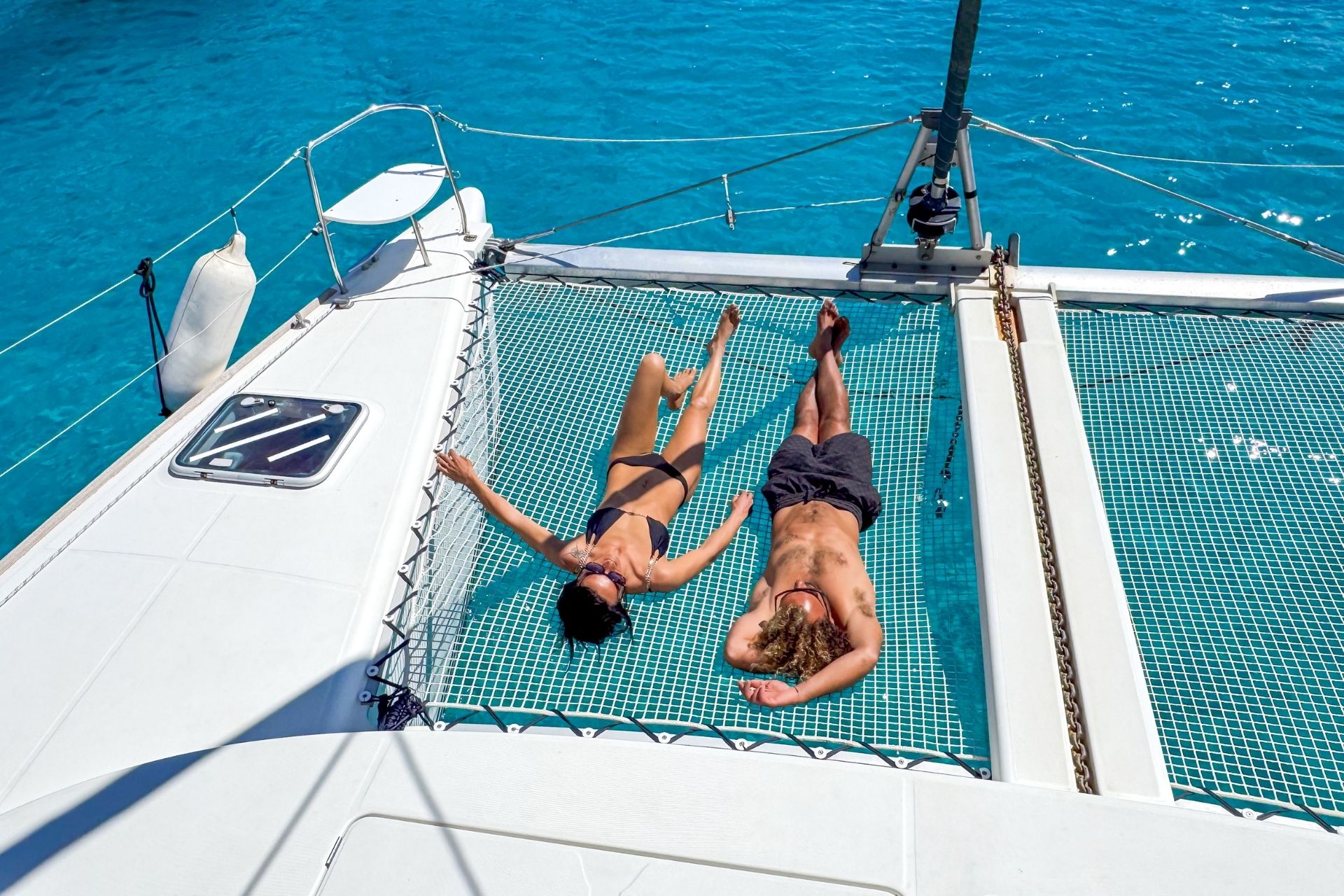 Two people relaxing on a catamaran in the middle of the sea, with an island in the background.