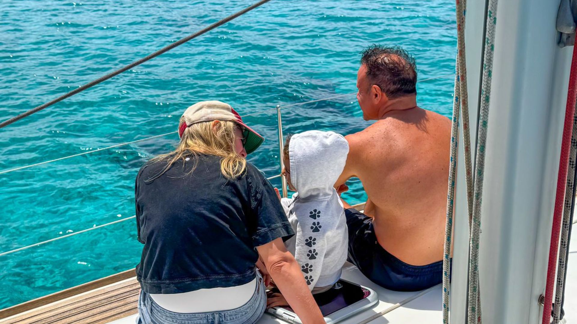 Tres personas en un barco miran el agua azul que tienen delante, probablemente durante una visita turística