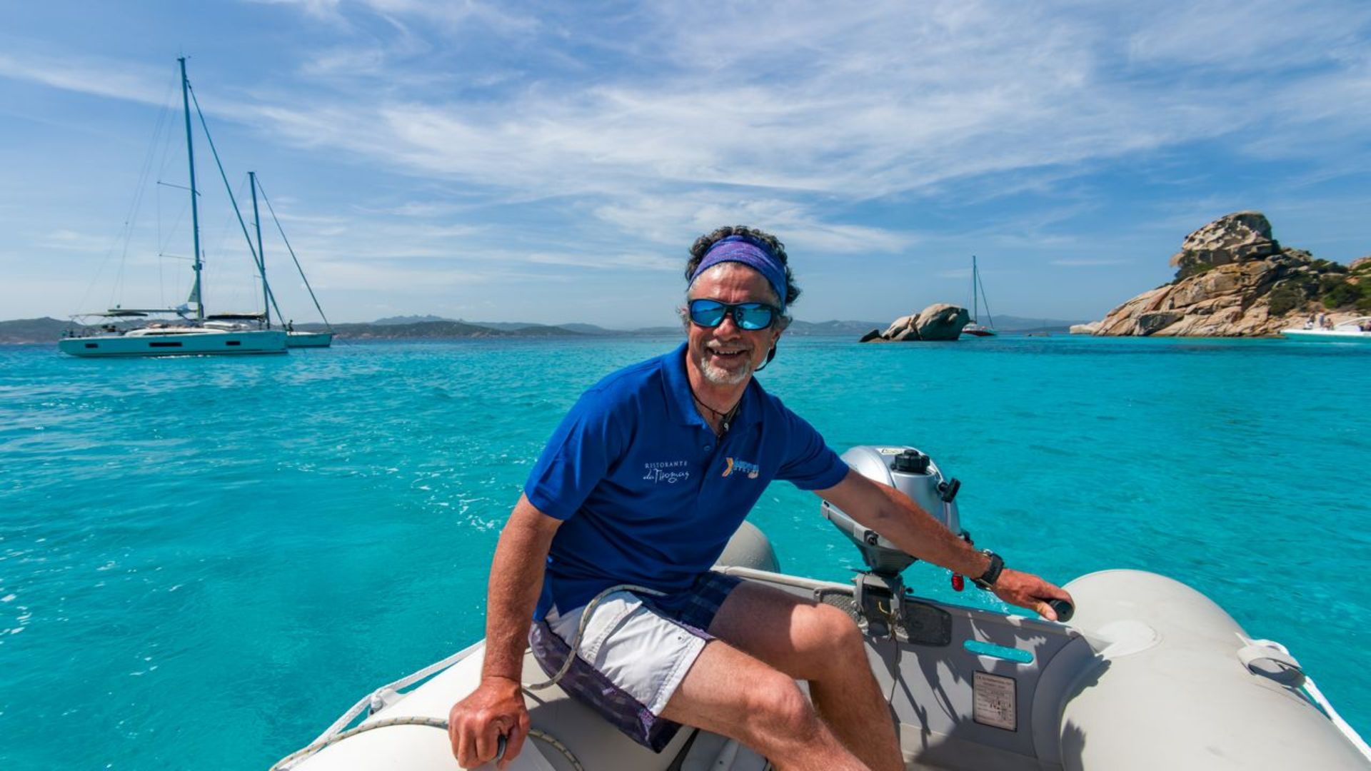 Hombre sentado en un barco con un fondo de mar azul e islas rocosas