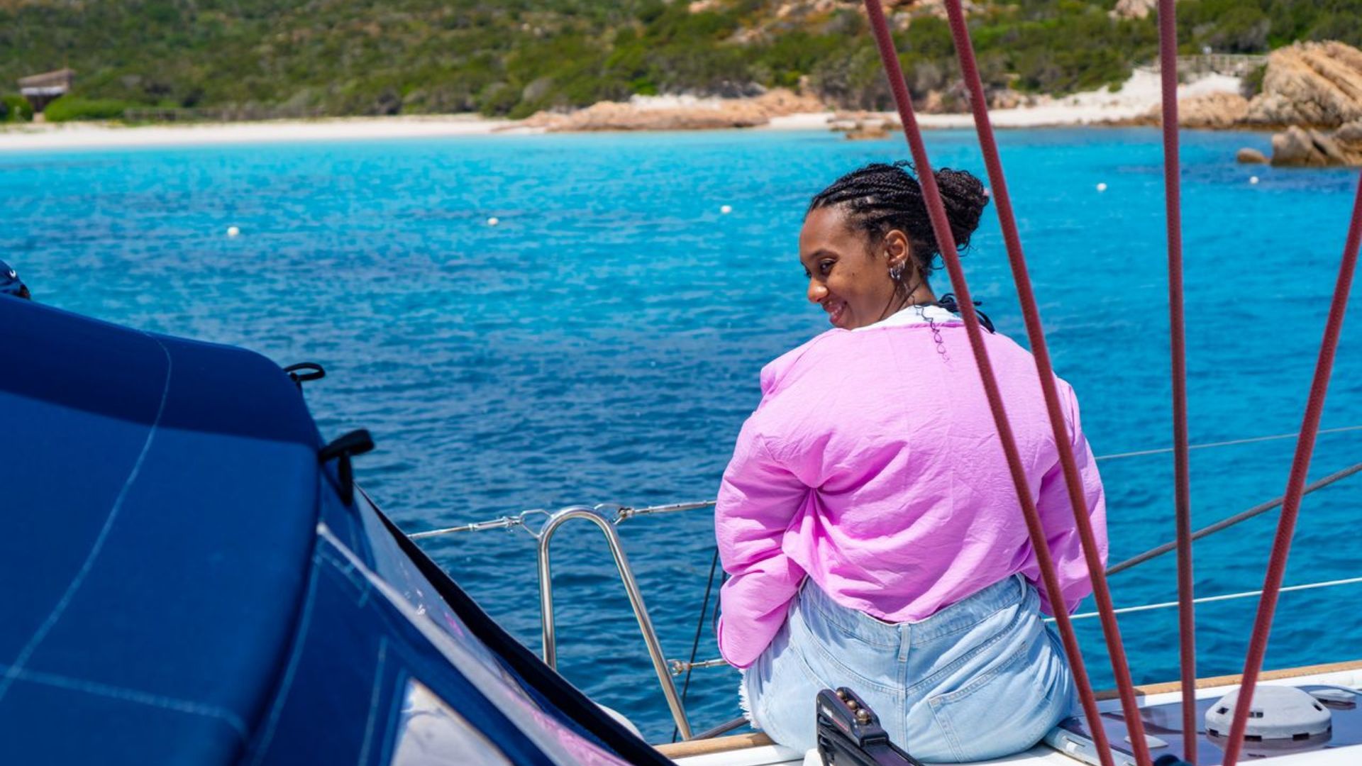 Una mujer sonríe sentada en un barco frente a un mar azul y una playa blanca