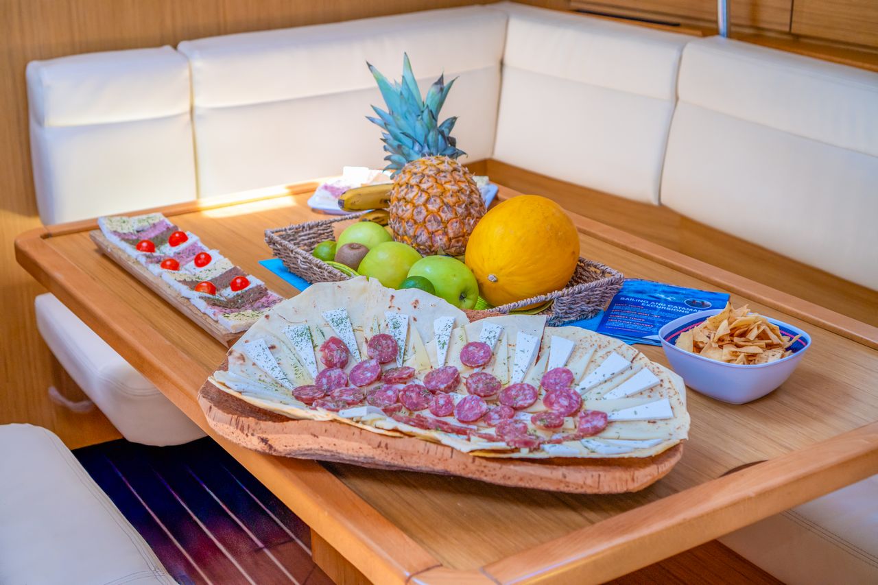 Mesa con comida y fruta sobre una mesa de barco con un fondo de mar cristalino e islas
