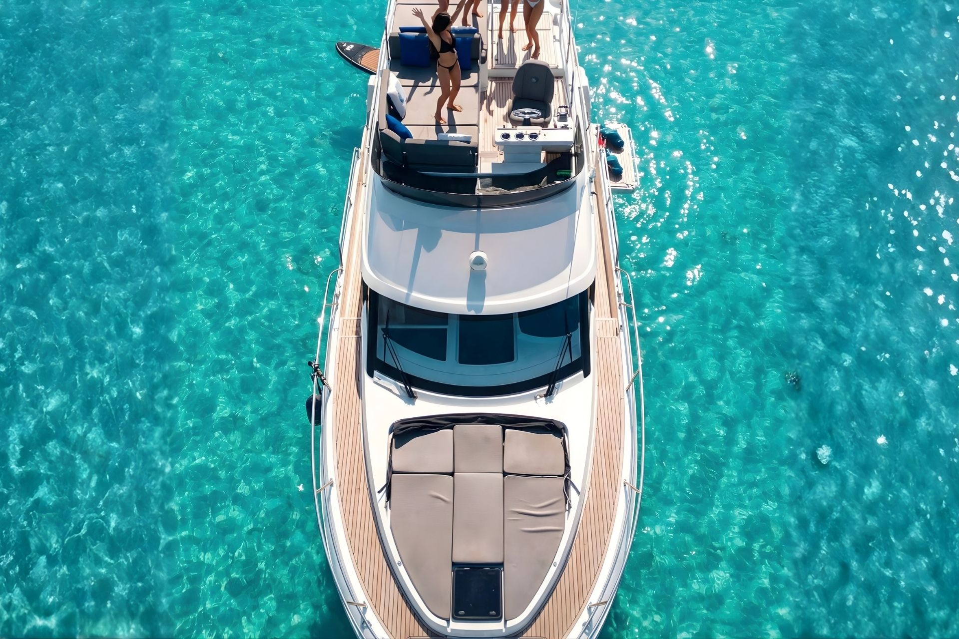 Private Yacht mit Passagieren in kristallklarem Wasser, in der Nähe einer Küste aus weißem und smaragdgrünem Sand.