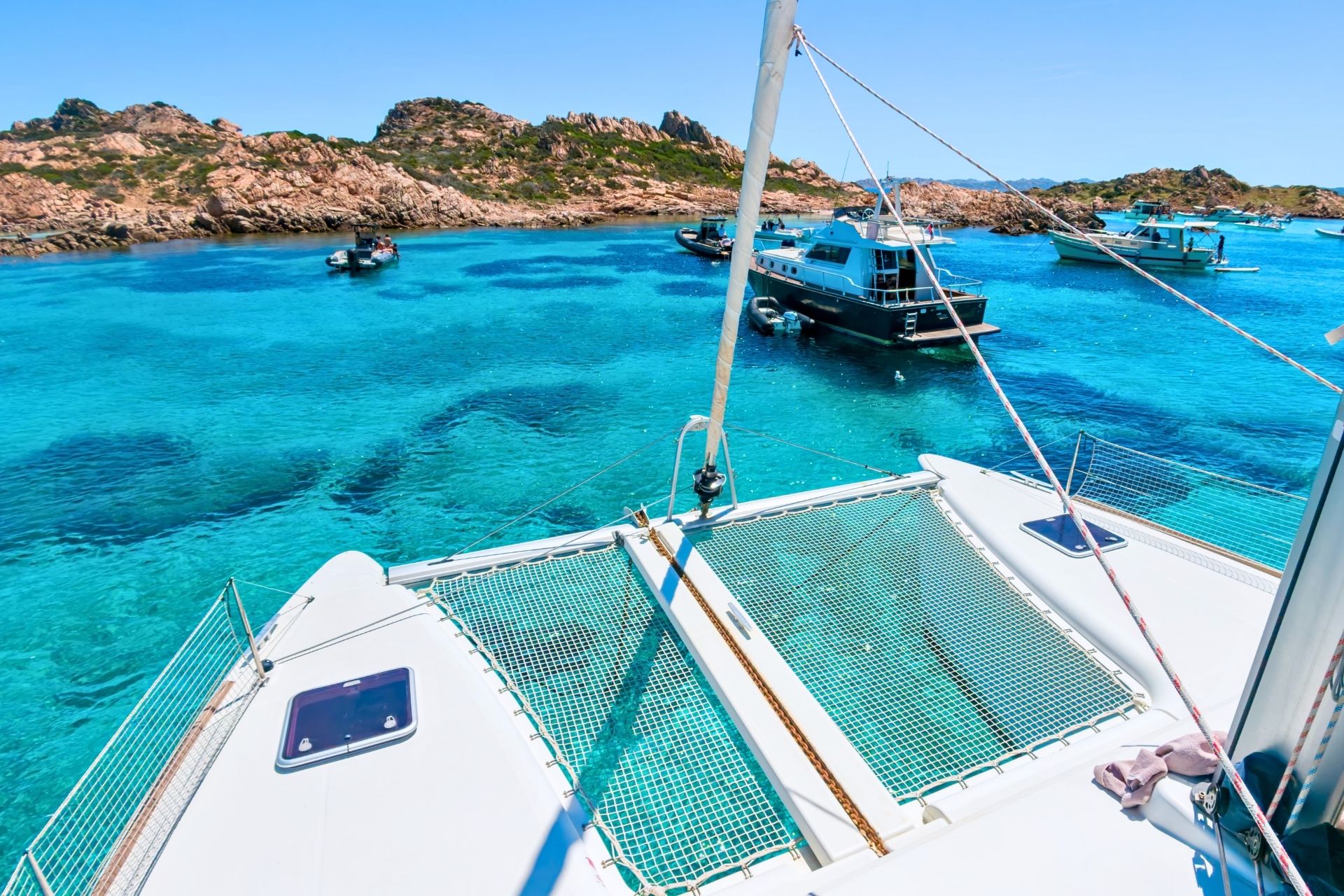 Image of a catamaran and other boats in a crystal clear sea with islands in the background.