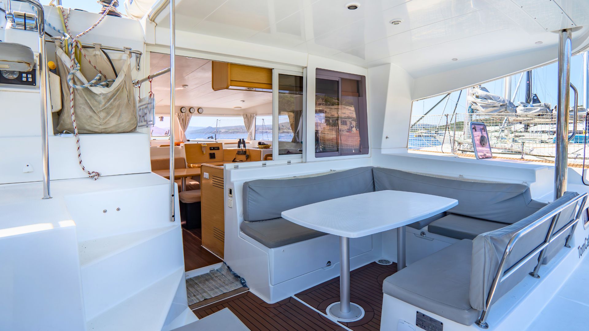 Interior de un catamarán con mesa y sofás, ventanas panorámicas y vista al mar
