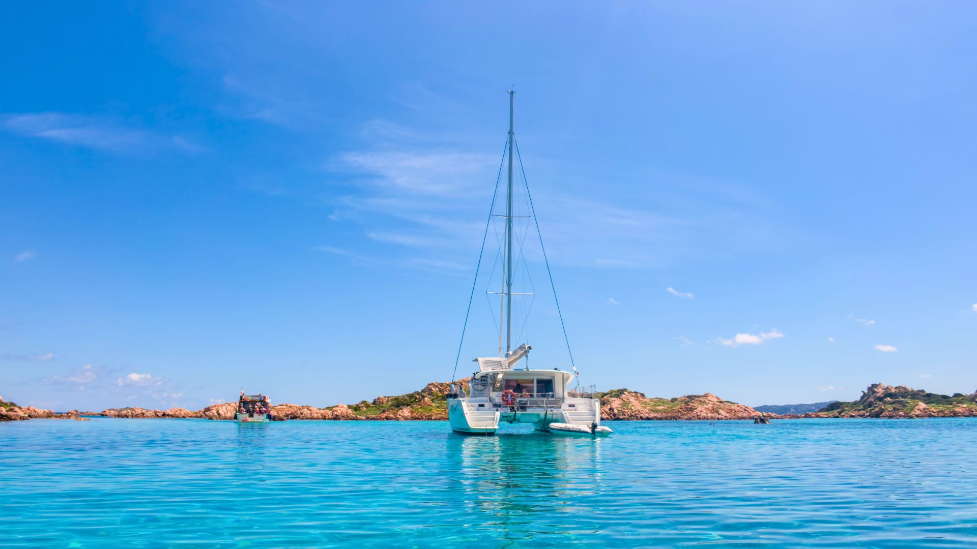 Imagen de un catamarán navegando en aguas cristalinas con islas al fondo