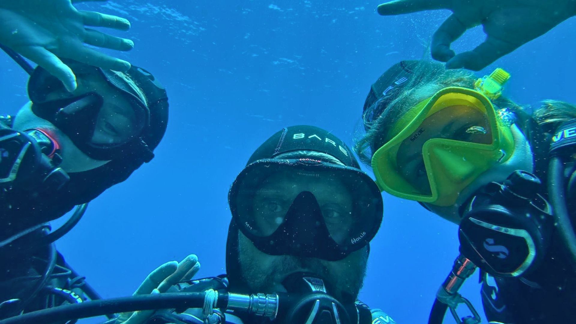 Three people in underwater clothing and masks, immersed in the clear waters of Sant'Antioco