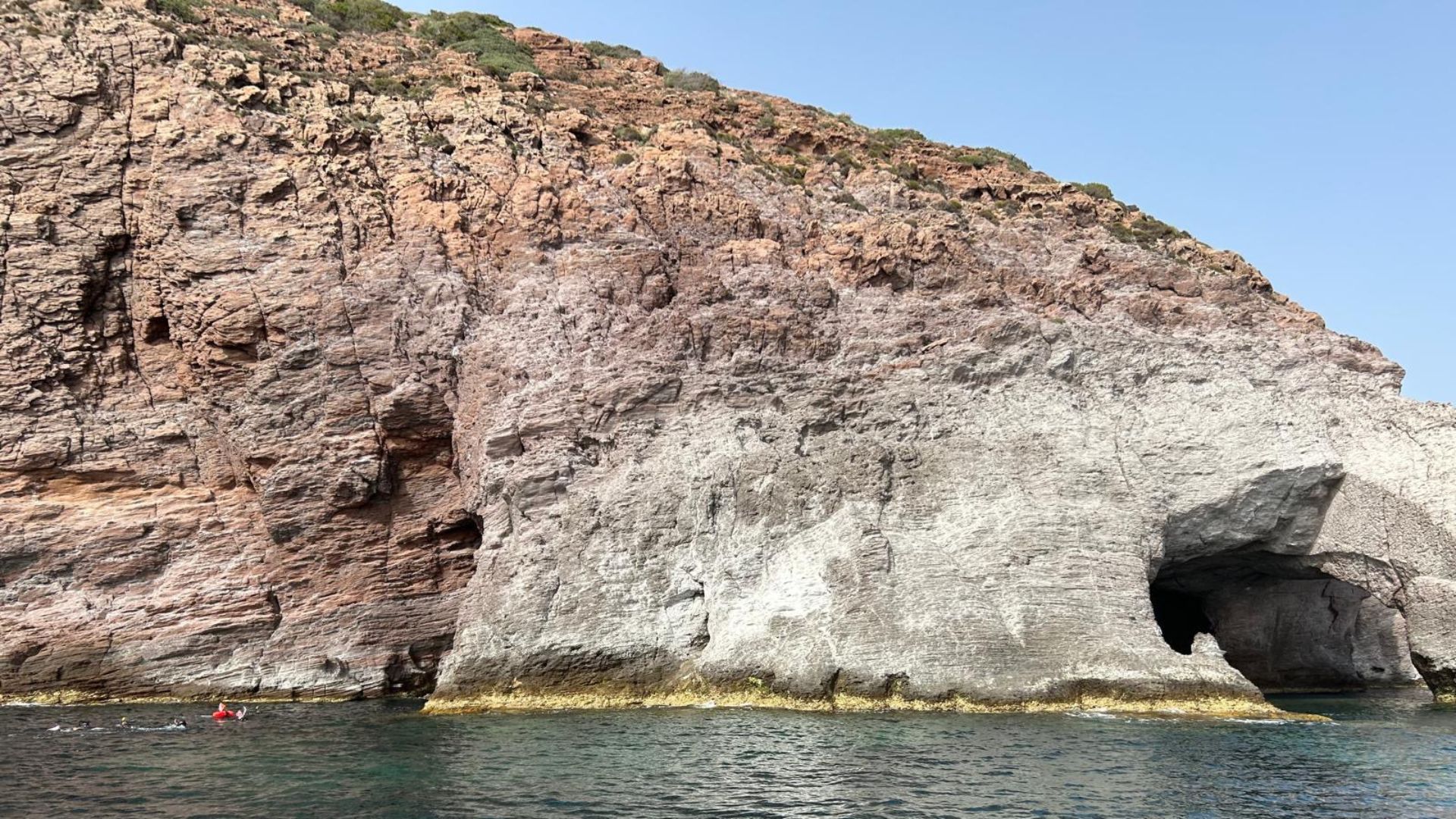 Imagen de una costa rocosa con una cueva natural y un grupo de personas buceando