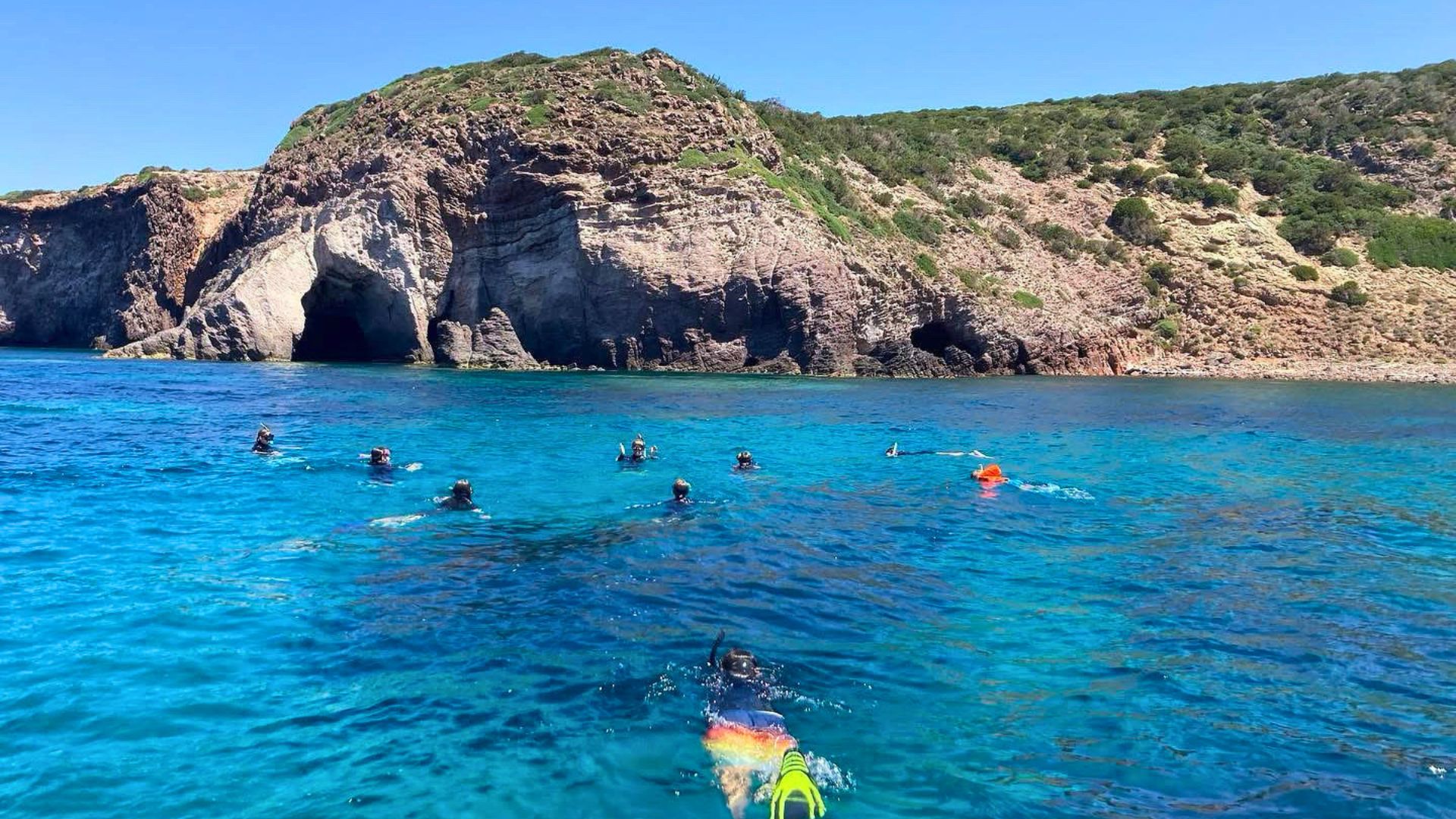 Gente buceando en el mar azul frente a un acantilado rocoso