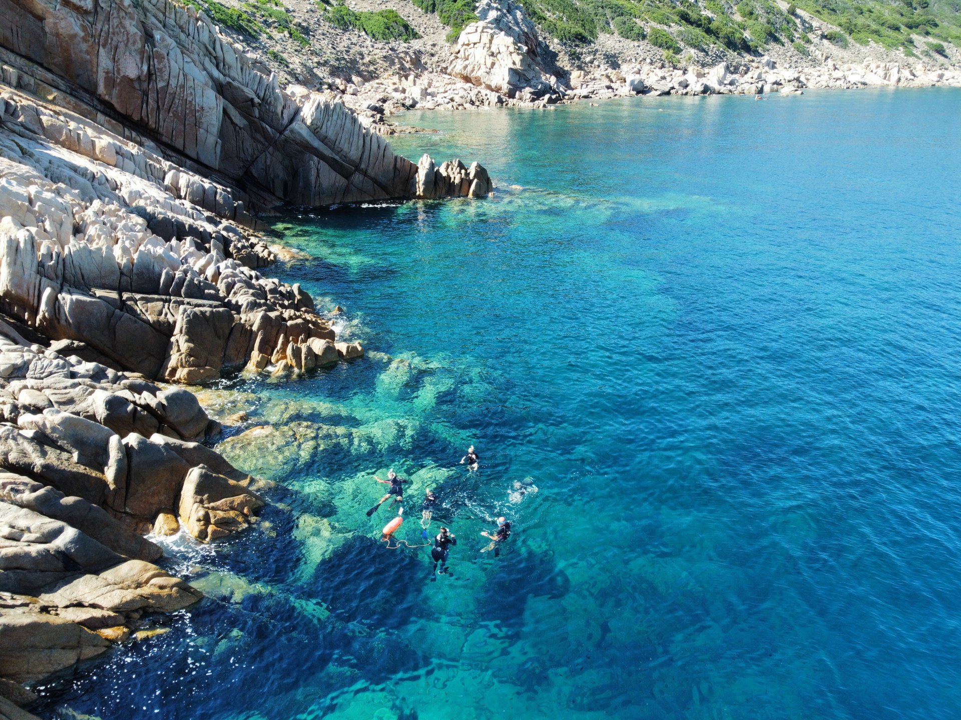Group of people snorkeling in crystal clear water near rocky cliffs at sunset