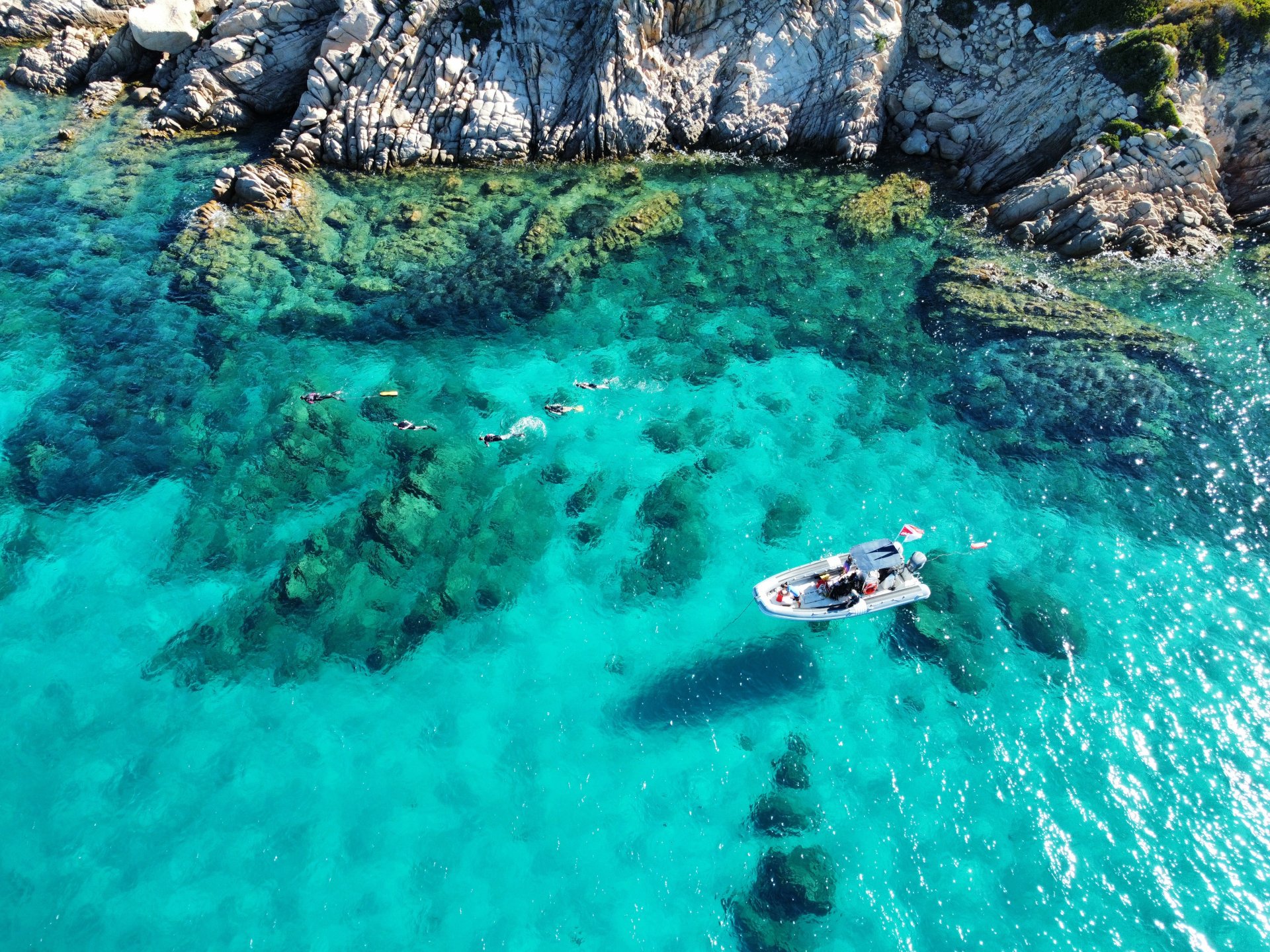 People snorkeling in clear, turquoise waters with spectacular cliffs in the background