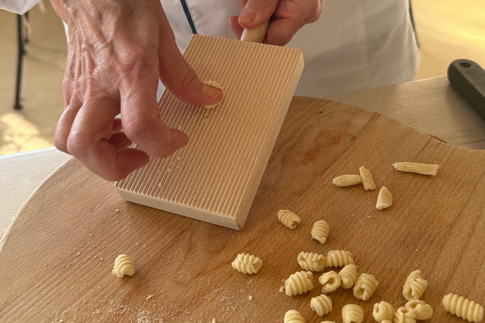 Una persona prepara pasta fresca con un utensile tradizionale in legno