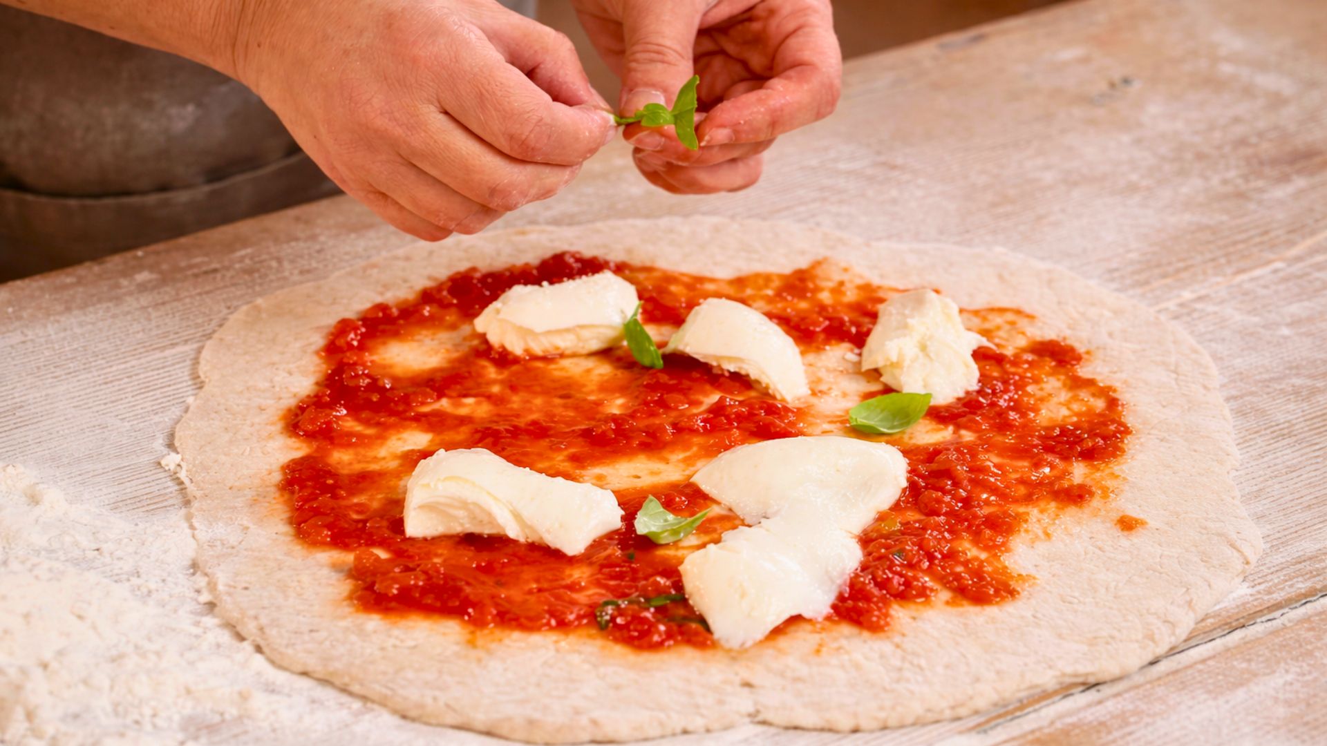 Una persona prepara una pizza con ingredienti freschi e basilico su un tavolo di legno