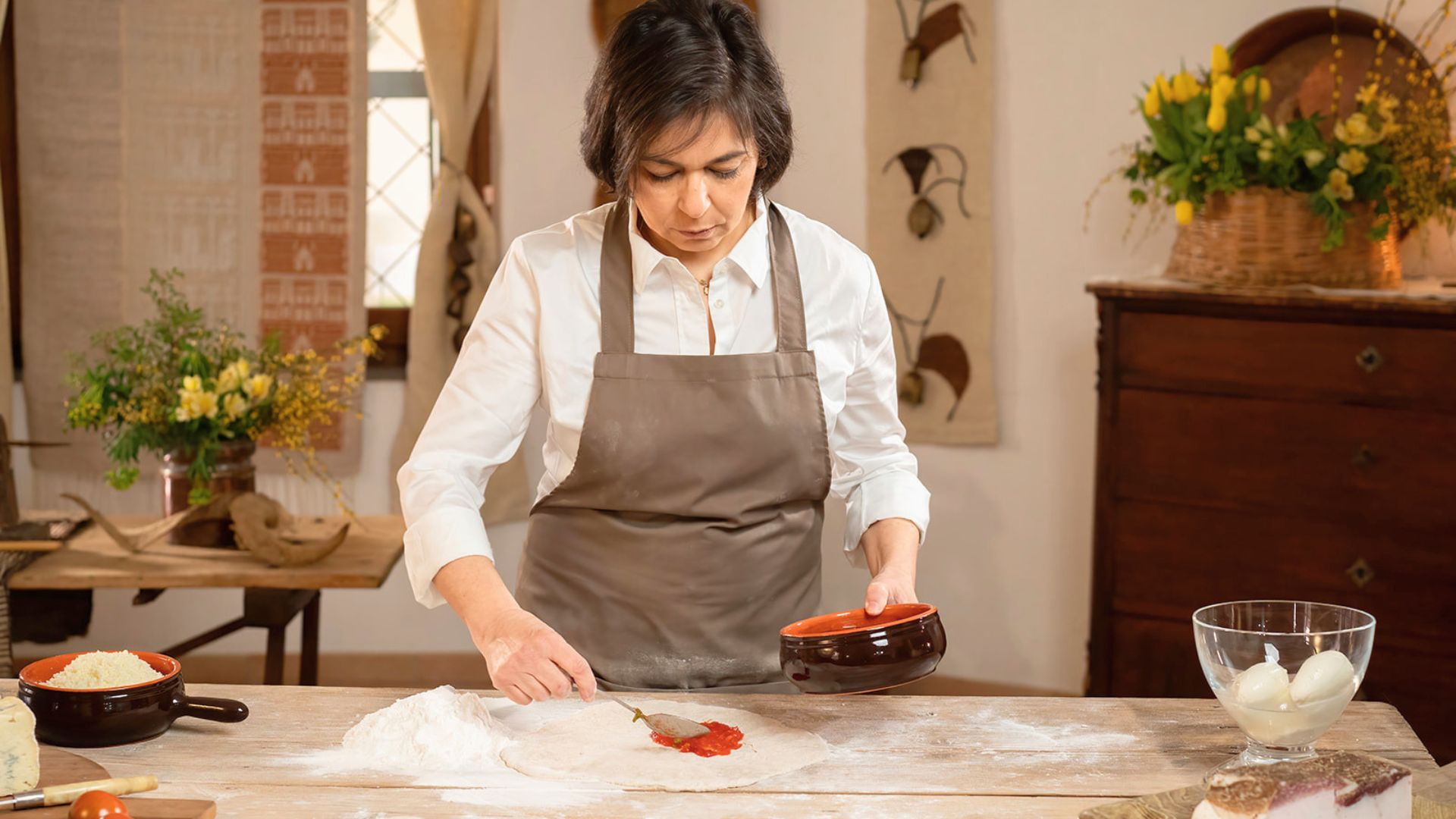 Una donna in cucina che prepara la pizza con ingredienti freschi su una tavola di legno