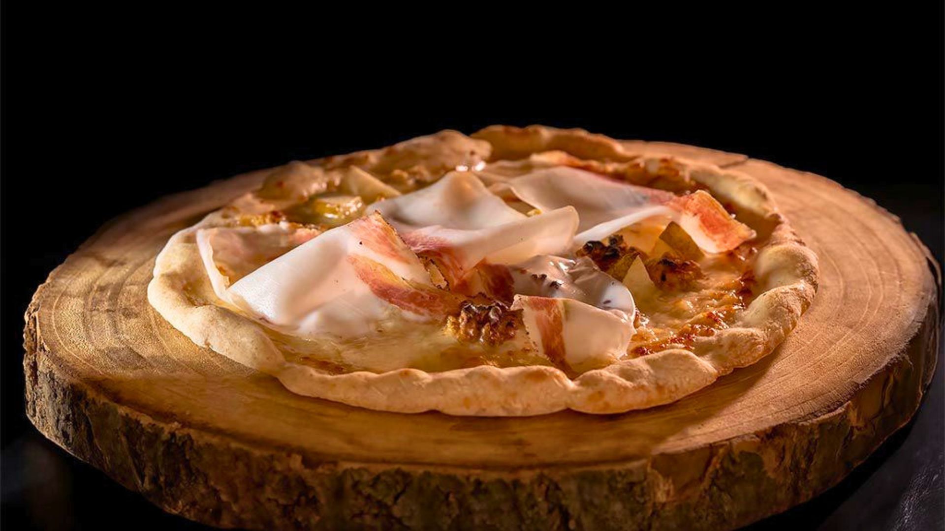 Una pizza con prosciutto e mozzarella su una base di legno