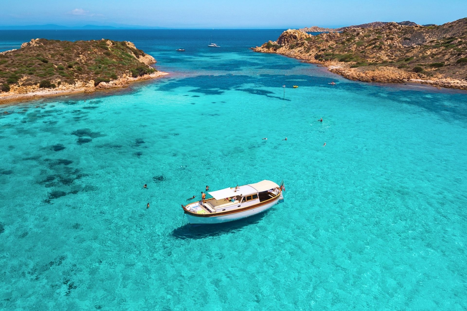 A vintage boat sails between the islands of Caprera, Budelli and Spargi with crystal clear sea and enchanting natural landscapes.