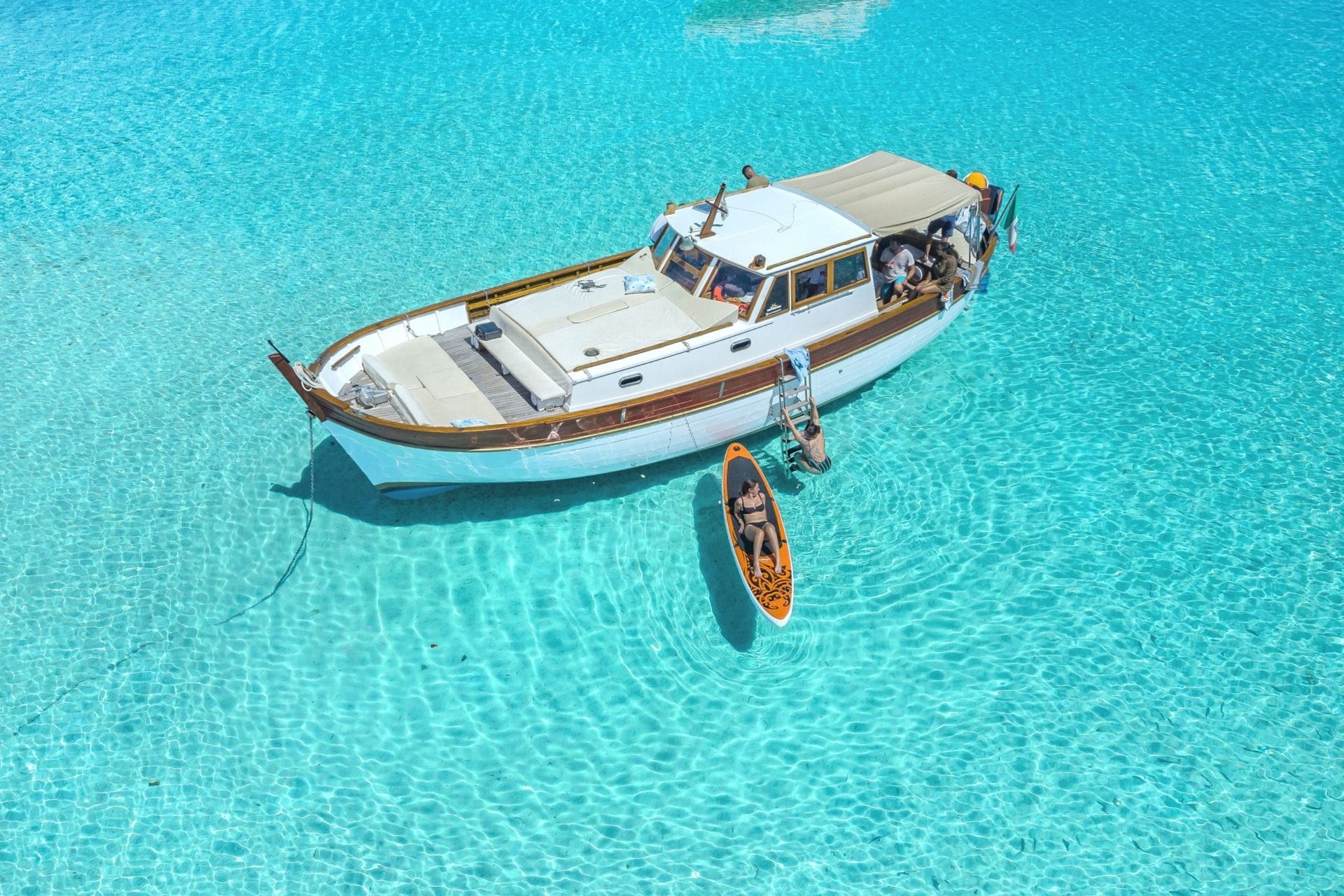 Vintage boat with people on board and in the water in a bay with crystal clear sea
