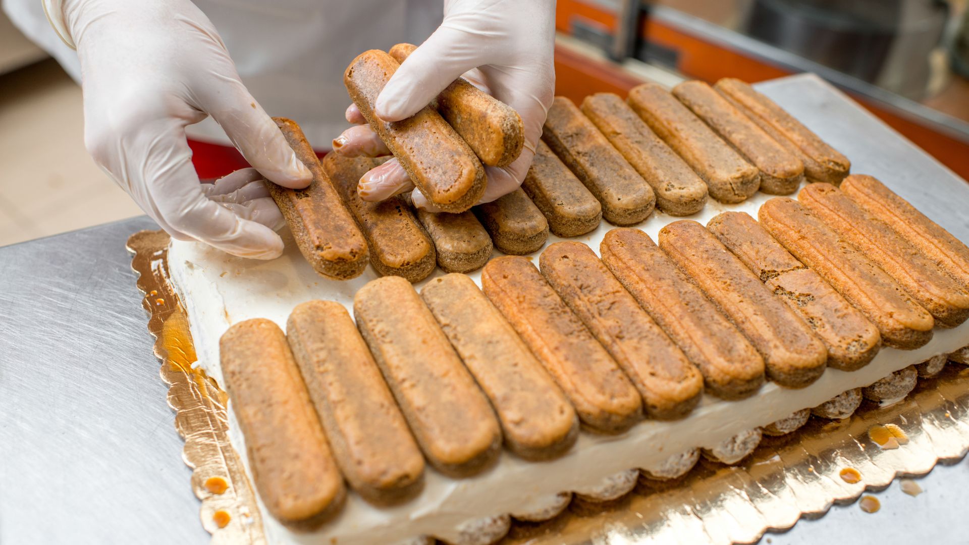 Person in white gloves placing cookies on top of a cake