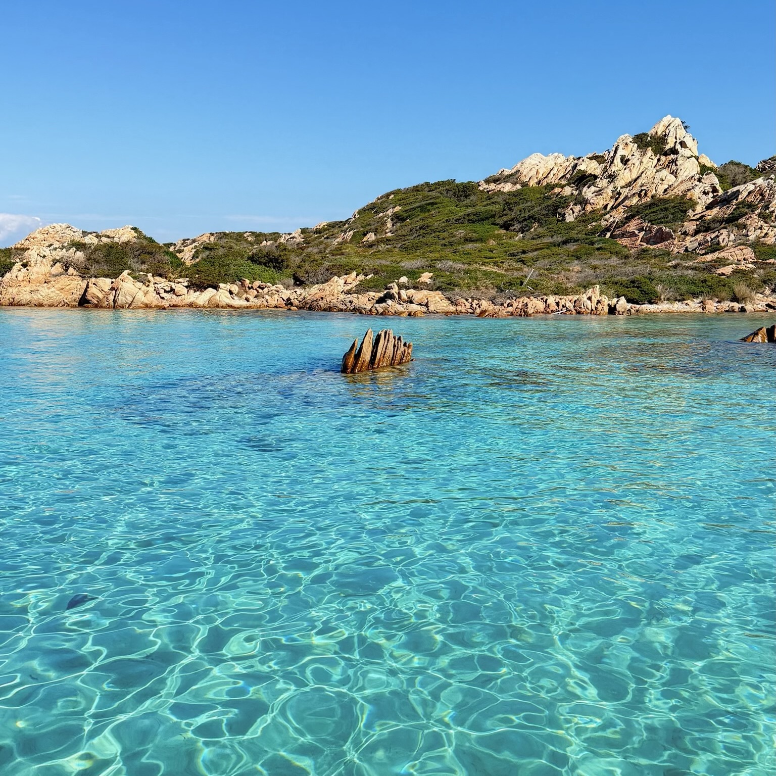 Bild eines Meeresgebiets mit klarem Wasser und aus dem Wasser ragenden Felsen, mit einer Insel im Hintergrund.