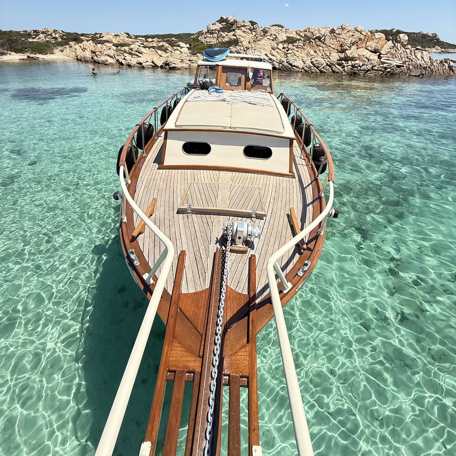 Bild einer hölzernen Gozzo, die in kristallklarem Wasser vor Anker liegt, mit Inseln im Hintergrund.