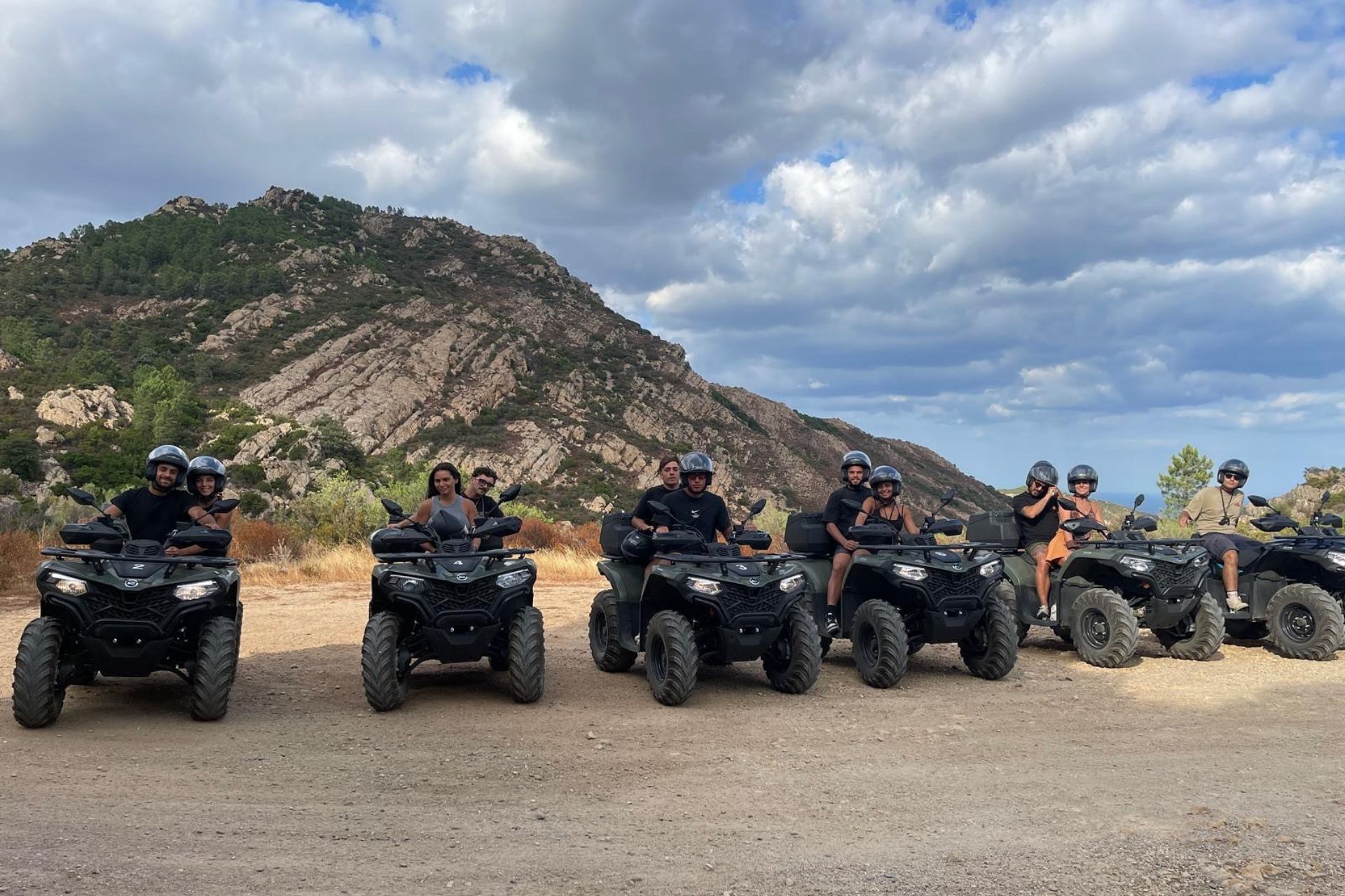 Groupe de personnes en quad sur un chemin de terre avec des montagnes en arrière-plan.