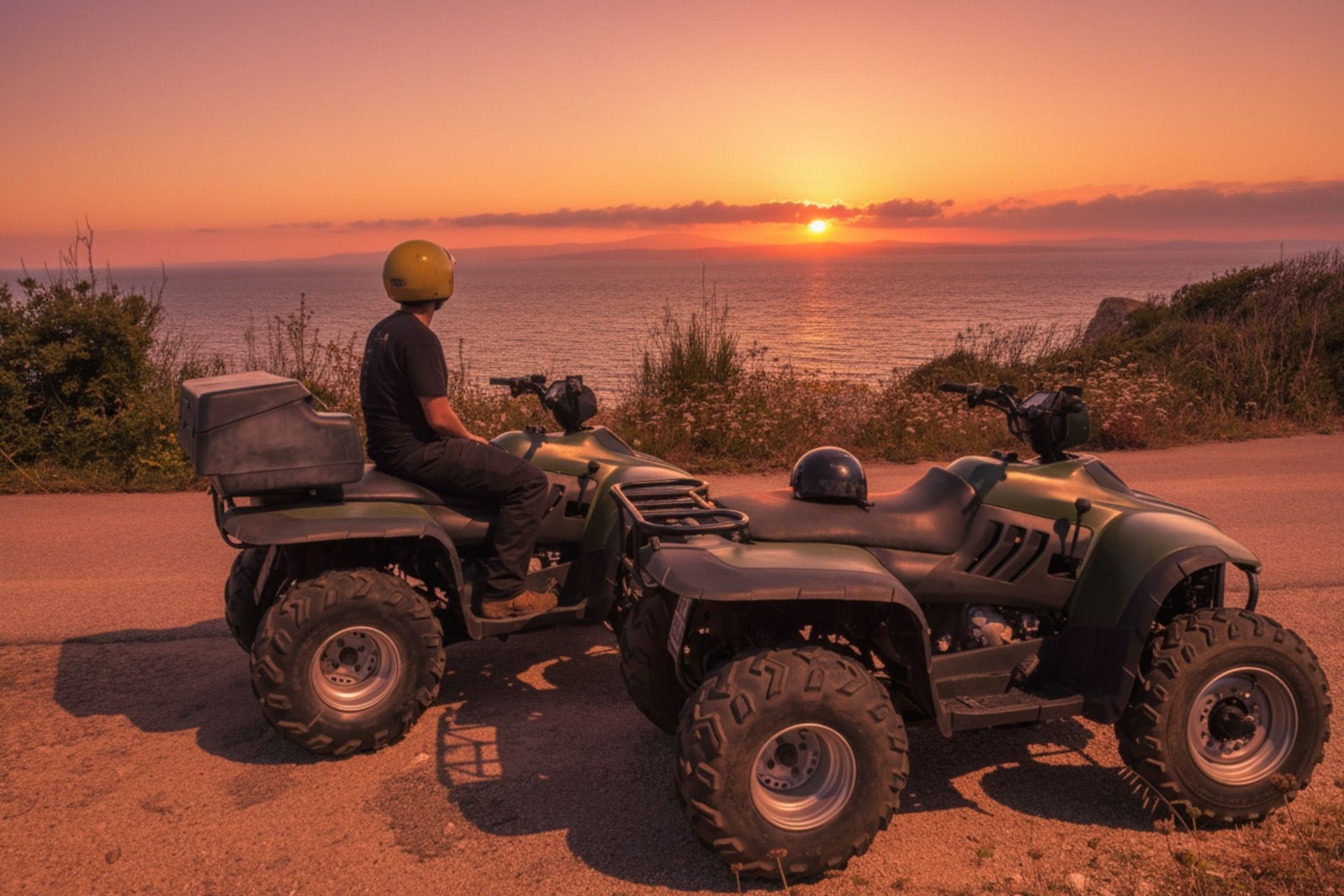 Deux VTT garés sur un chemin avec vue sur la mer au coucher du soleil. Un homme porte un casque jaune et est assis dans l'un des véhicules.