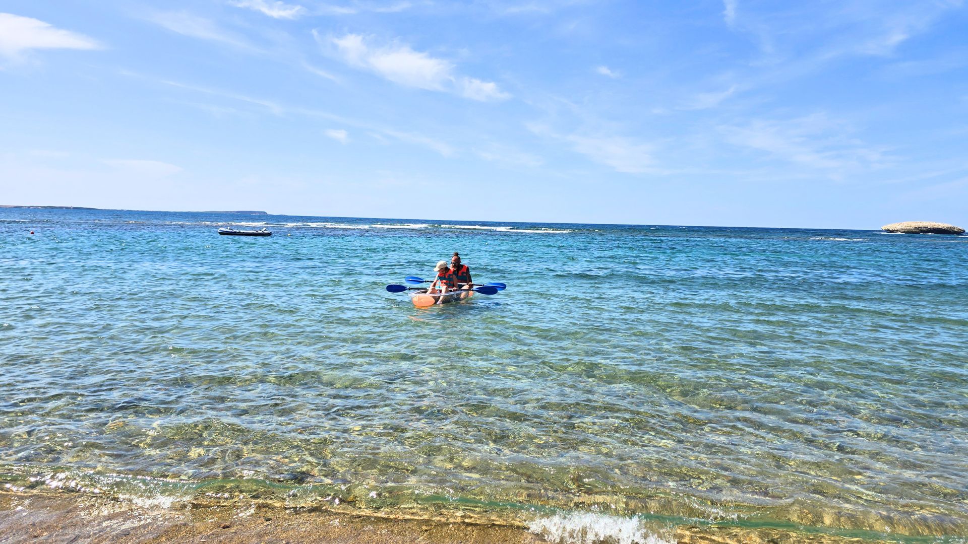 Due persone in un kayak trasparente, con pagaie blu, in acqua cristallina con fondo visibile