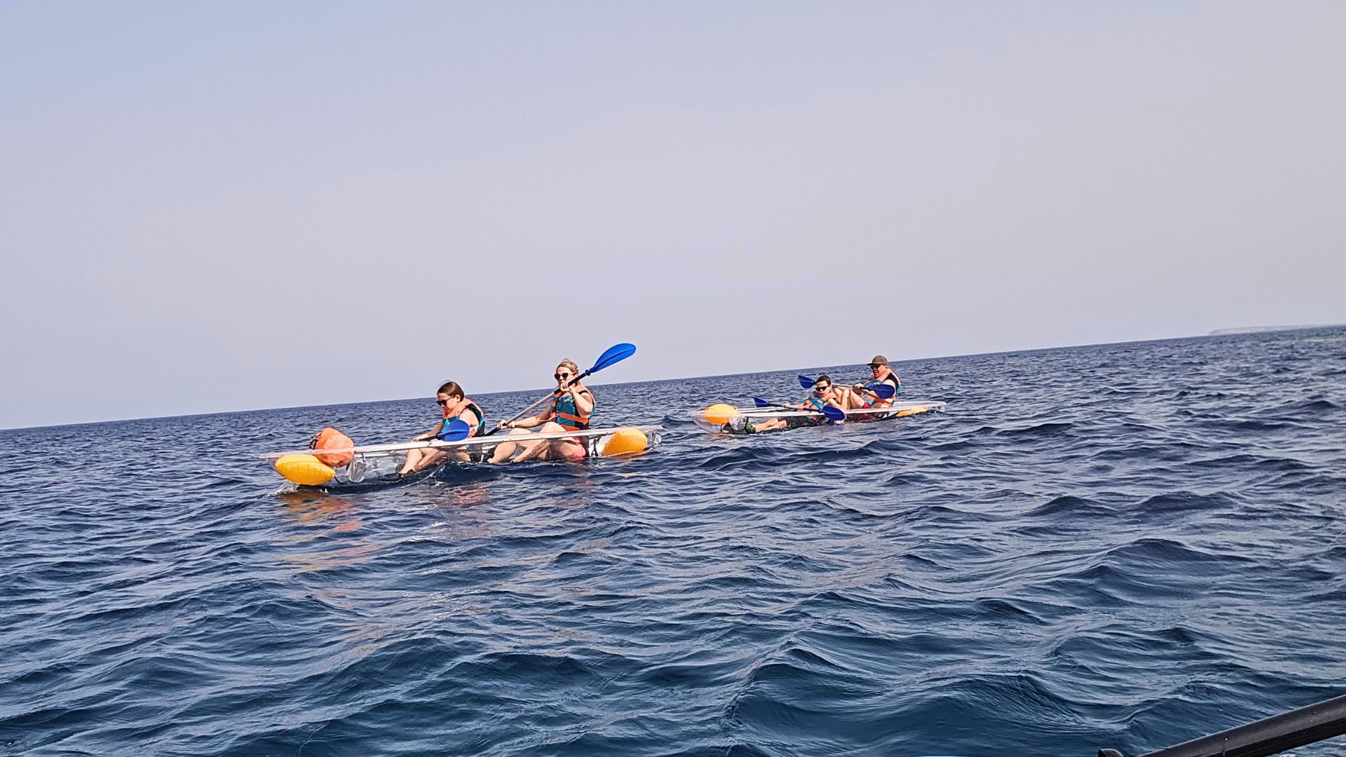Immagine di un gruppo di persone in kayak trasparente, pagaiando lungo la costa occidentale della Sardegna, vicino a Oristano. Le persone indossano giubbotti di salvataggio e utilizzano pagaie blu