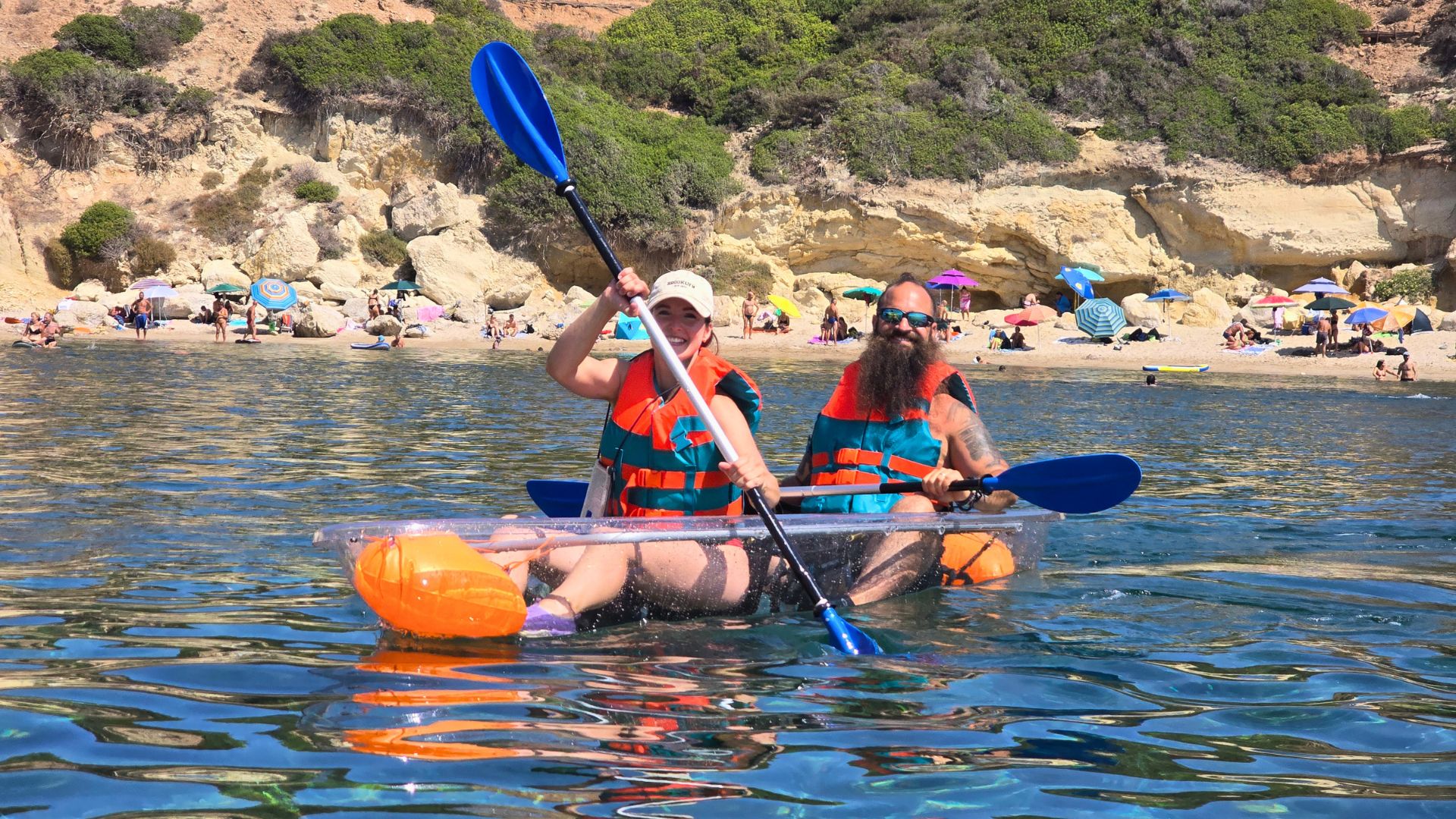Due persone in un kayak trasparente, in acqua, con un paesaggio naturale sullo sfondo