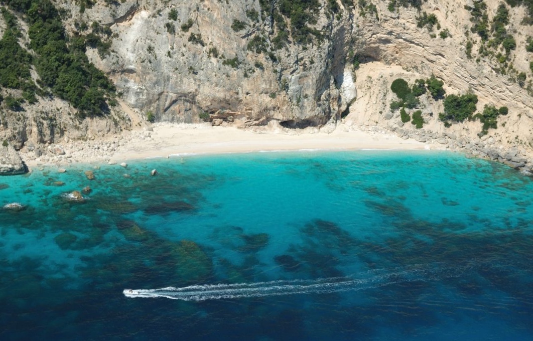 Navega en catamarán en un mar azul con una costa rocosa y una playa blanca.