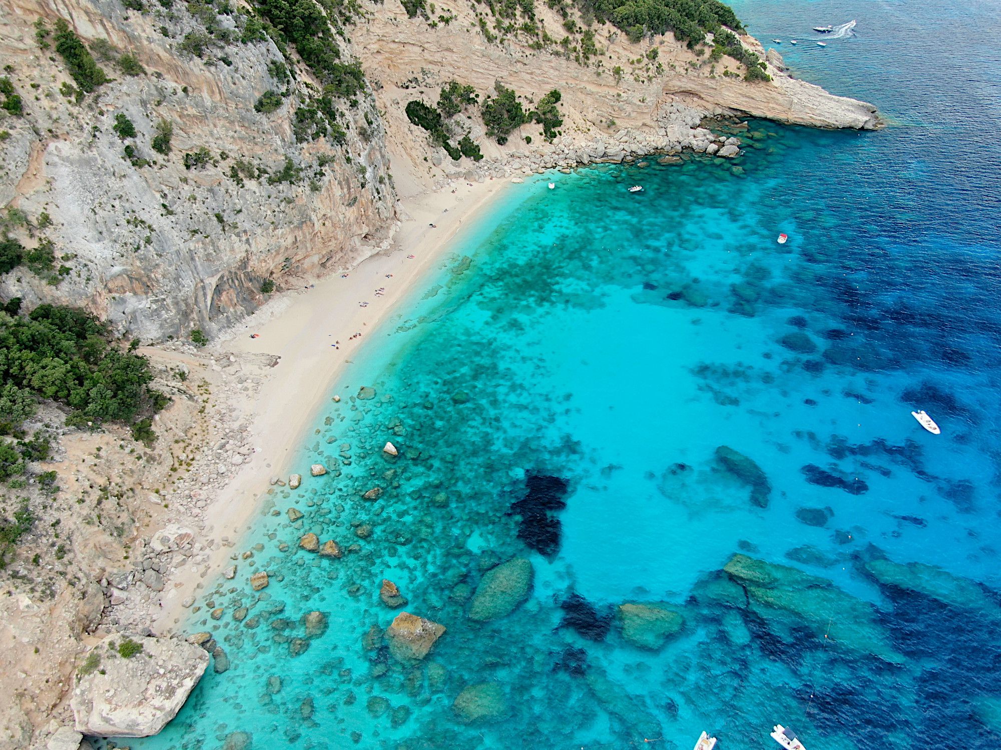 Vista aérea de una playa con acantilados de granito y mar cristalino, ideal para paseos en catamarán.