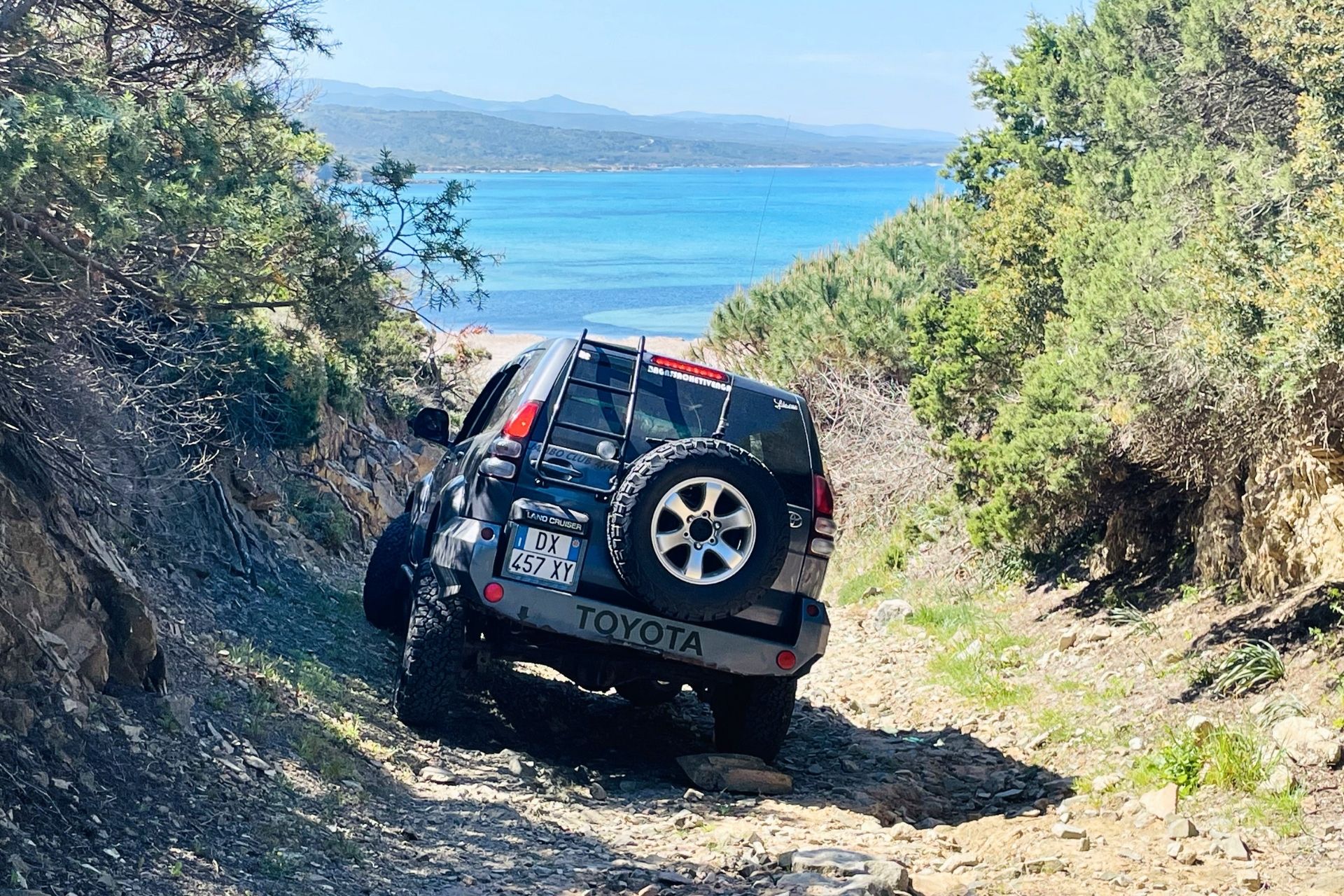 An off-road vehicle travels along a natural path between granite hills and Mediterranean scrub.