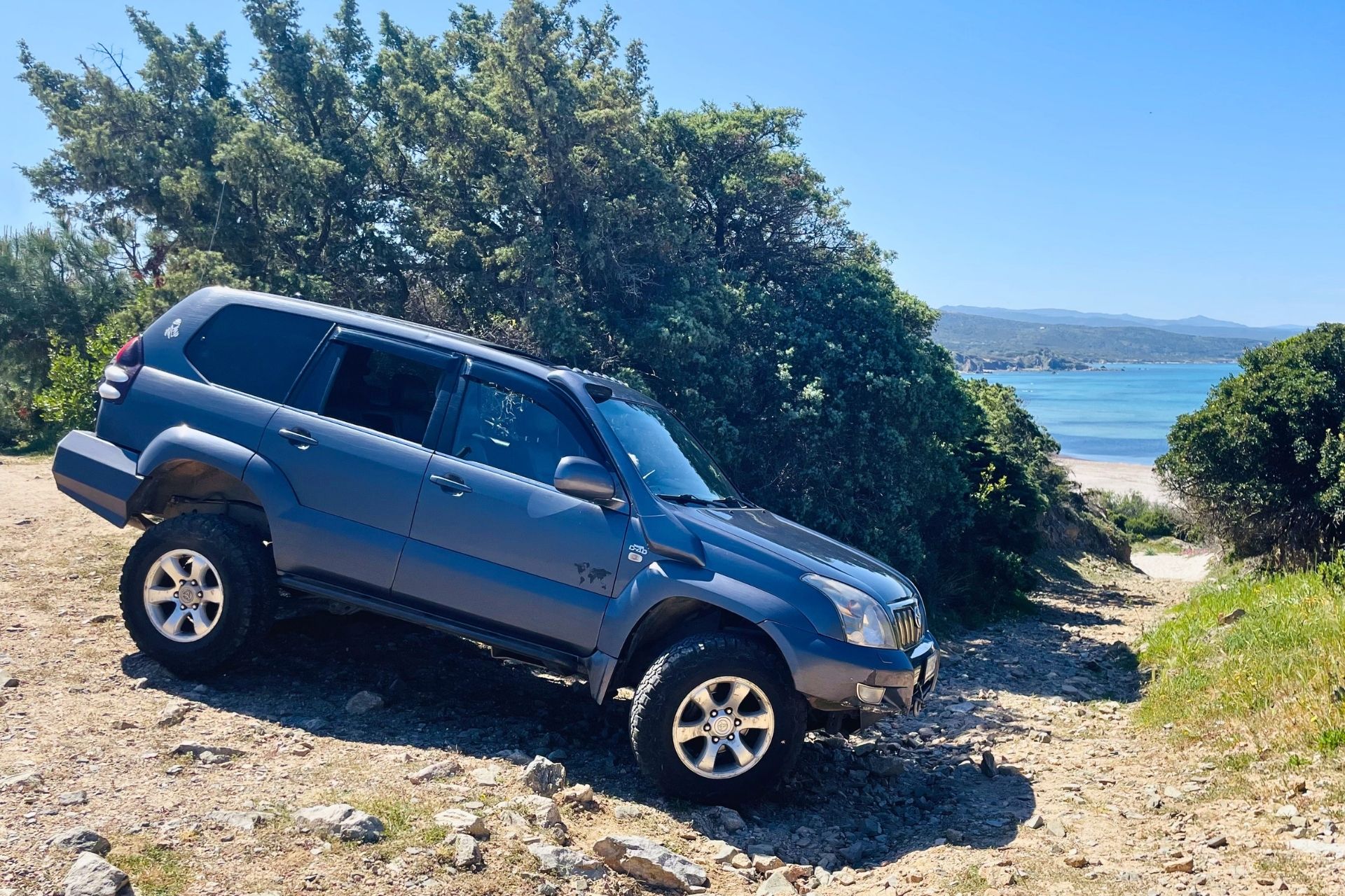 An off-road vehicle navigates a dirt path through pristine landscapes with a view of the sea and the island of Maddalena.