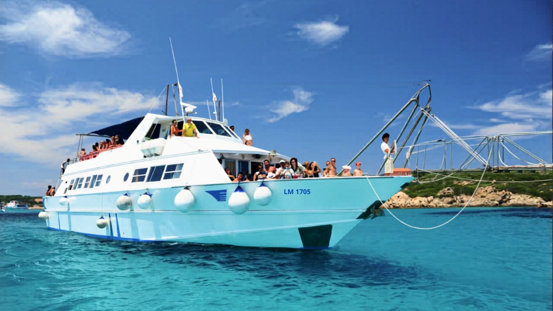 Un bateau à moteur avec des passagers dans l'eau bleue, avec des îles en arrière-plan et un pont sur la droite