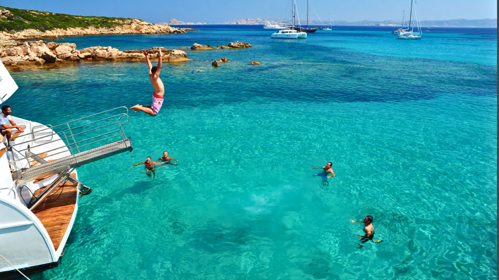 Image de personnes plongeant dans la mer depuis un bateau, entourées d'îles et de falaises