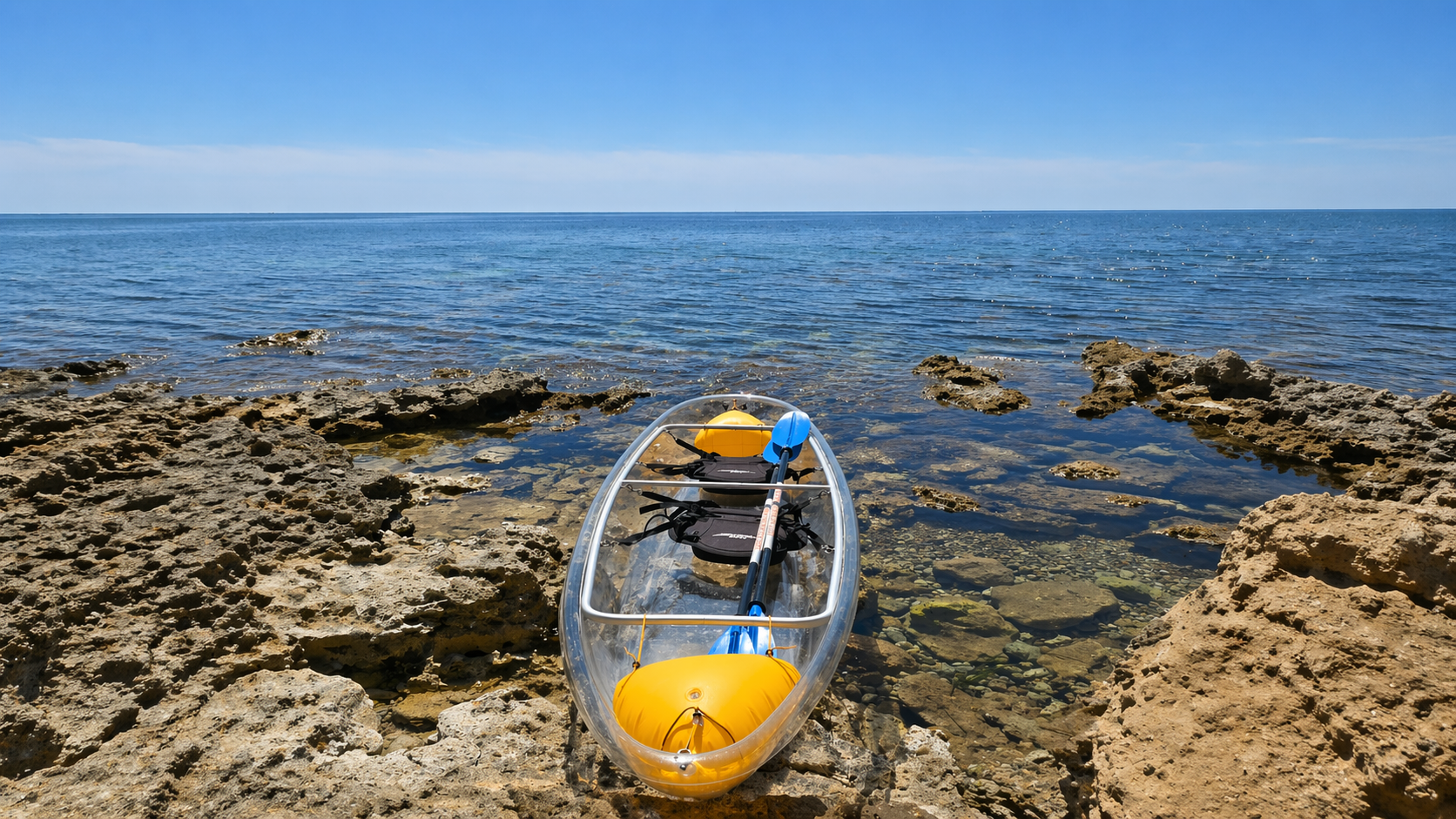 Un kayak trasparente parcheggiato su rocce con il mare calmo sullo sfondo