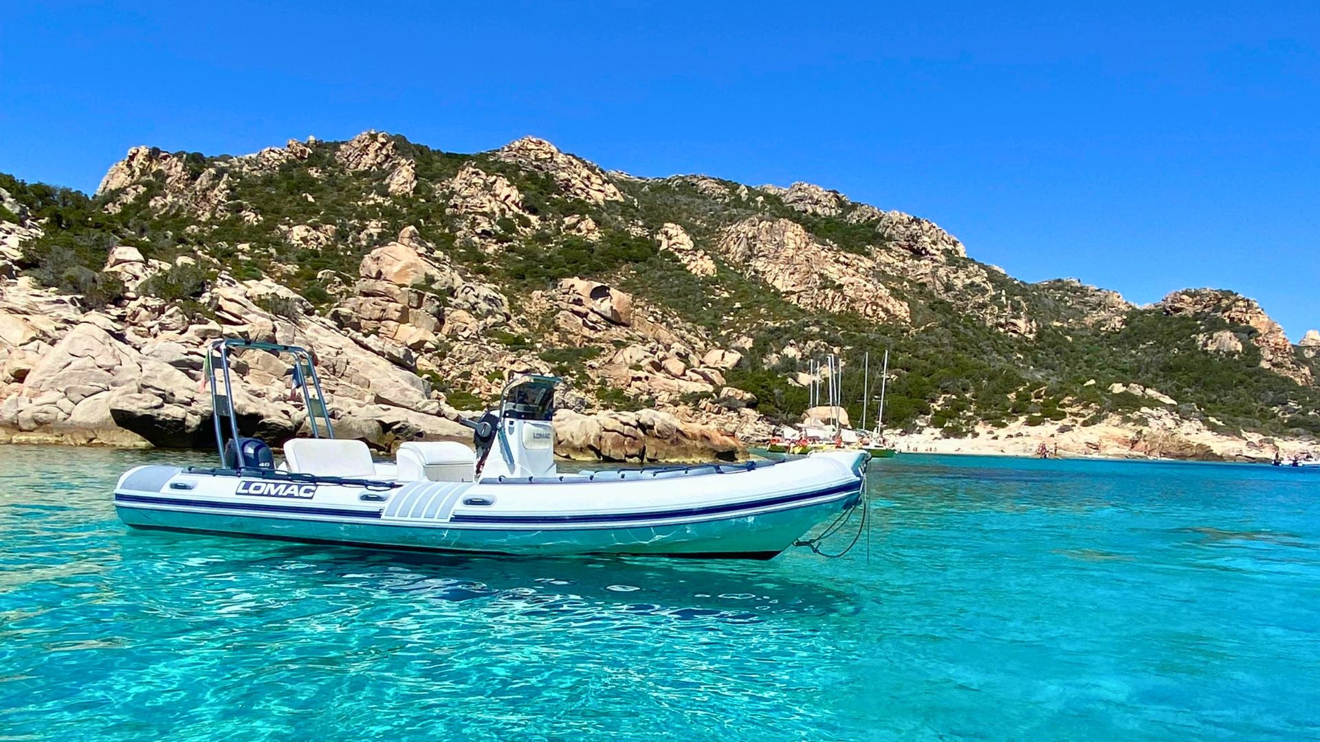 Immagine di un gommone ormeggiato in acque cristalline con scogliere granitiche sullo sfondo