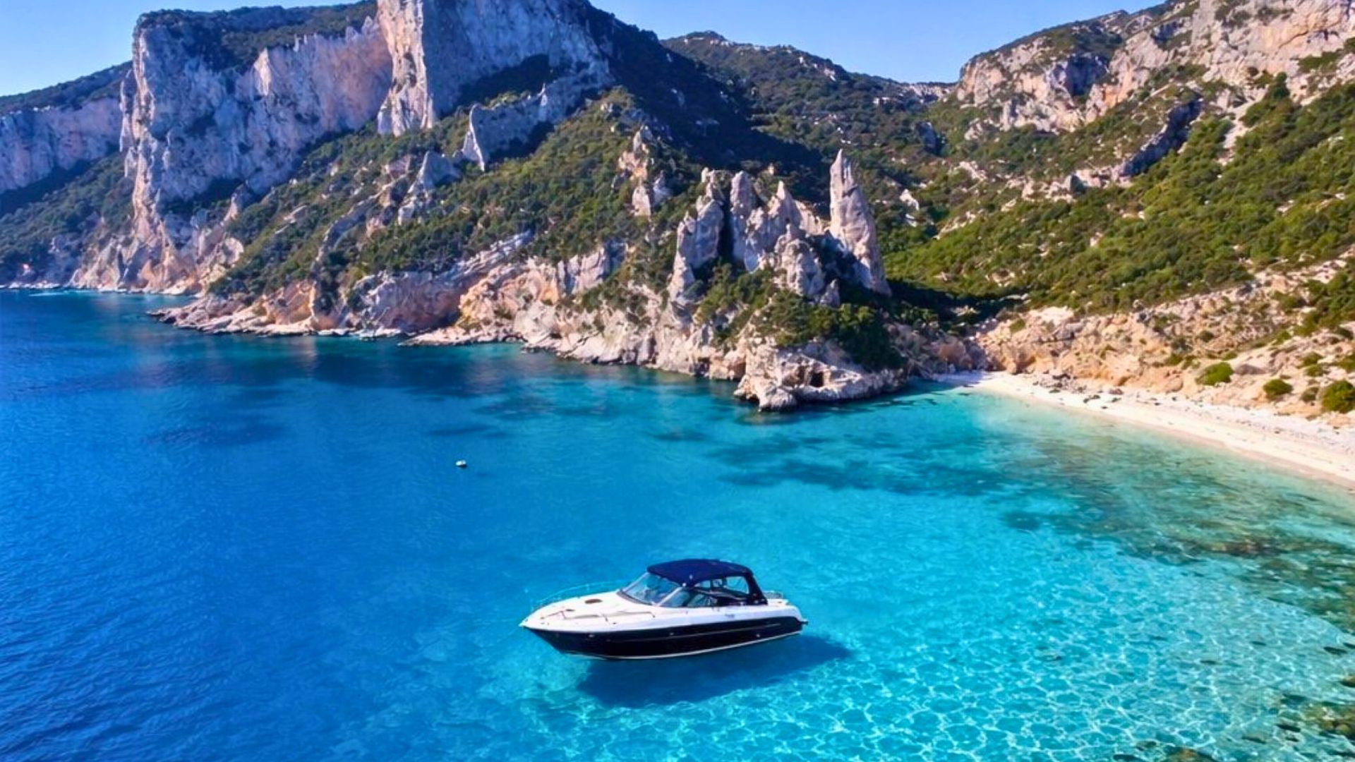 Ein Boot segelt in kristallklarem Wasser in der Nähe einer Küste mit Klippen und einem weißen Strand