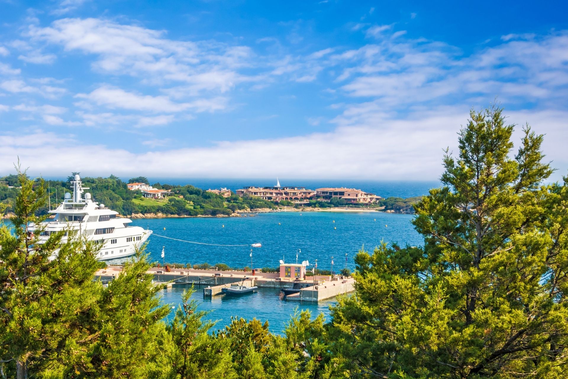 Picture of a marina with a large moored yacht and a small pier with boats and a building on the shore.