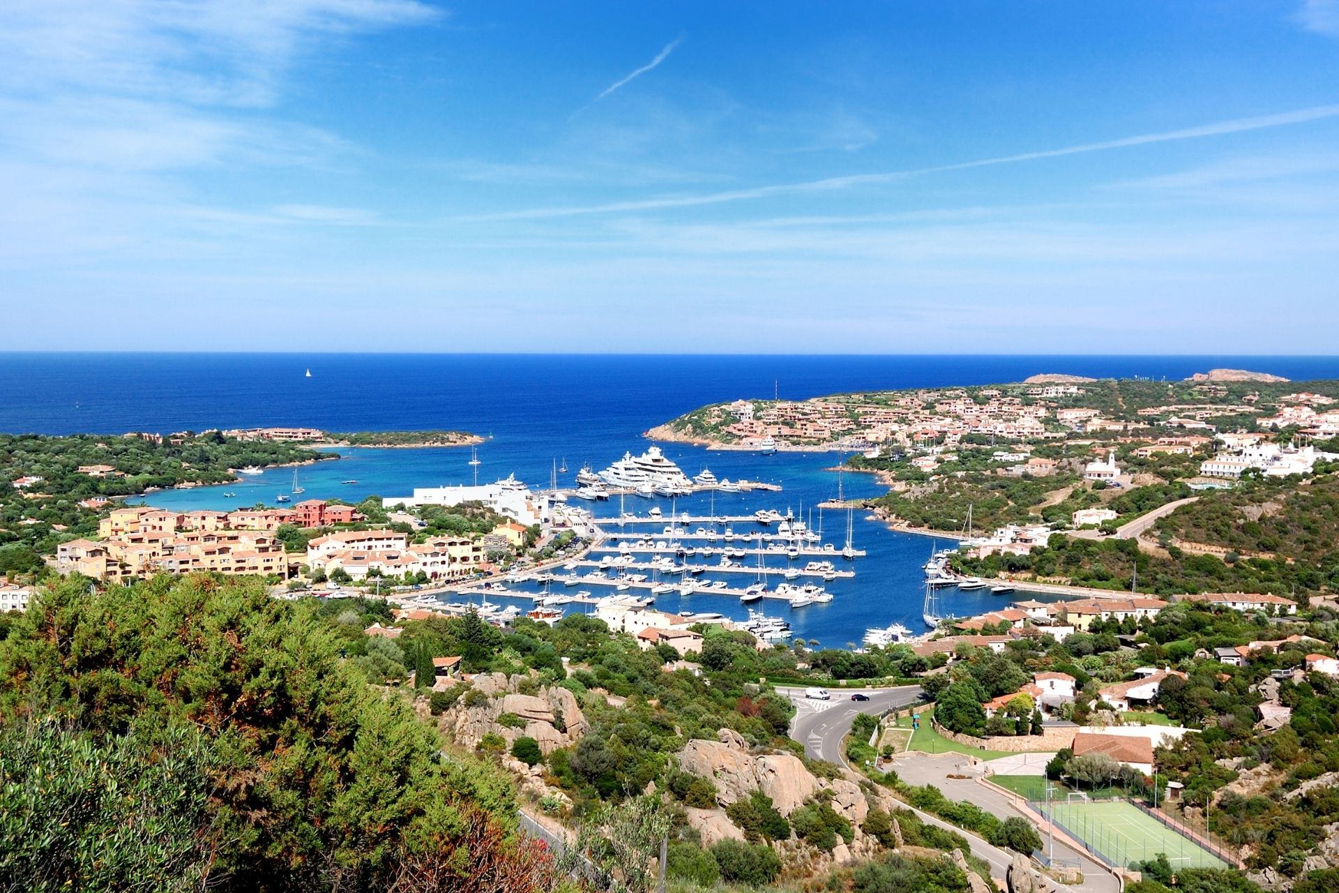 Aerial view of a coastal resort with a marina and a panoramic road.